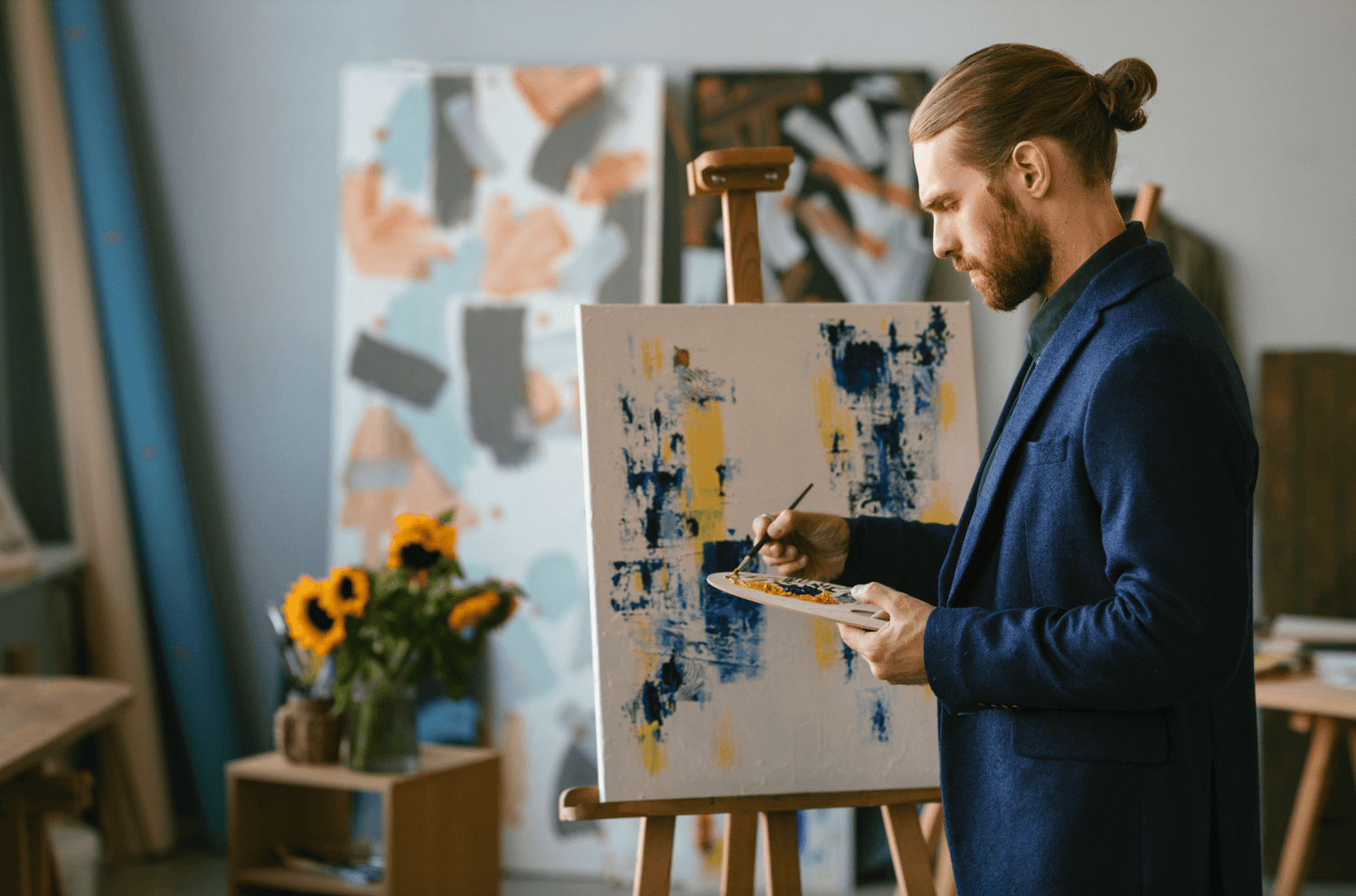 Artiste peignant sur toile avec palette, dans un studio créatif rempli de œuvres colorées
