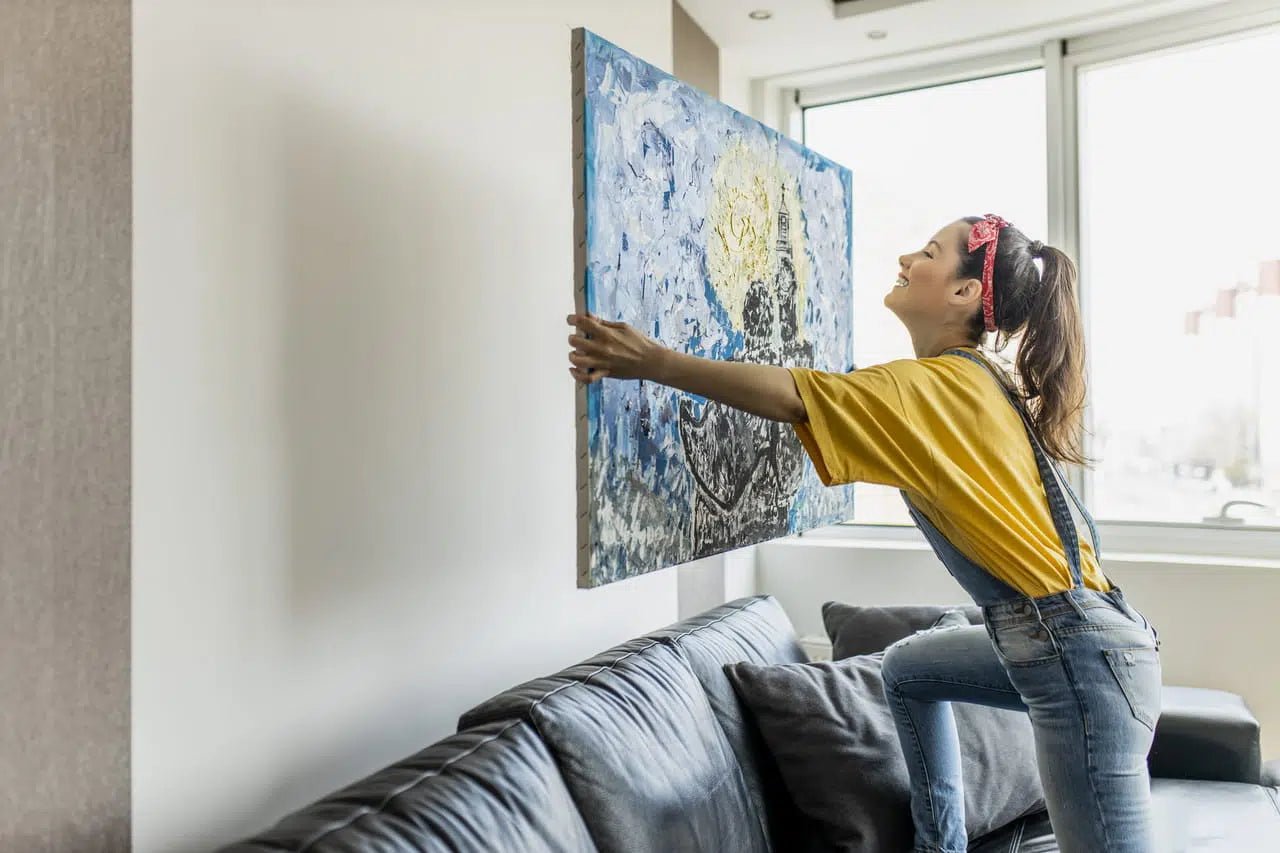 Jeune fille accrochant une peinture colorée sur un mur dans un salon moderne