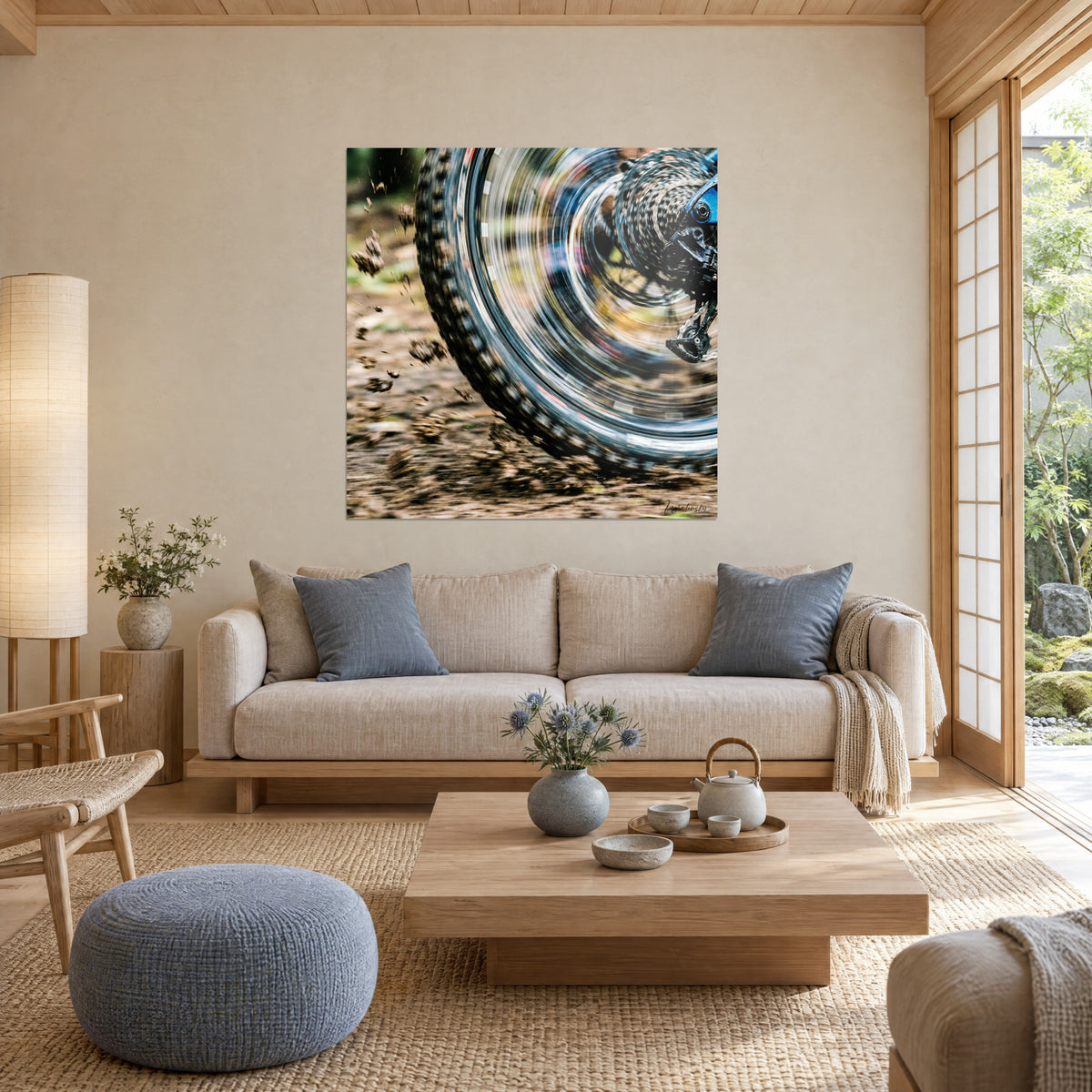 Wall art of a knobby mountain bike tire at full speed, brown mud splashes and blue frame, above a sofa in a bright living room