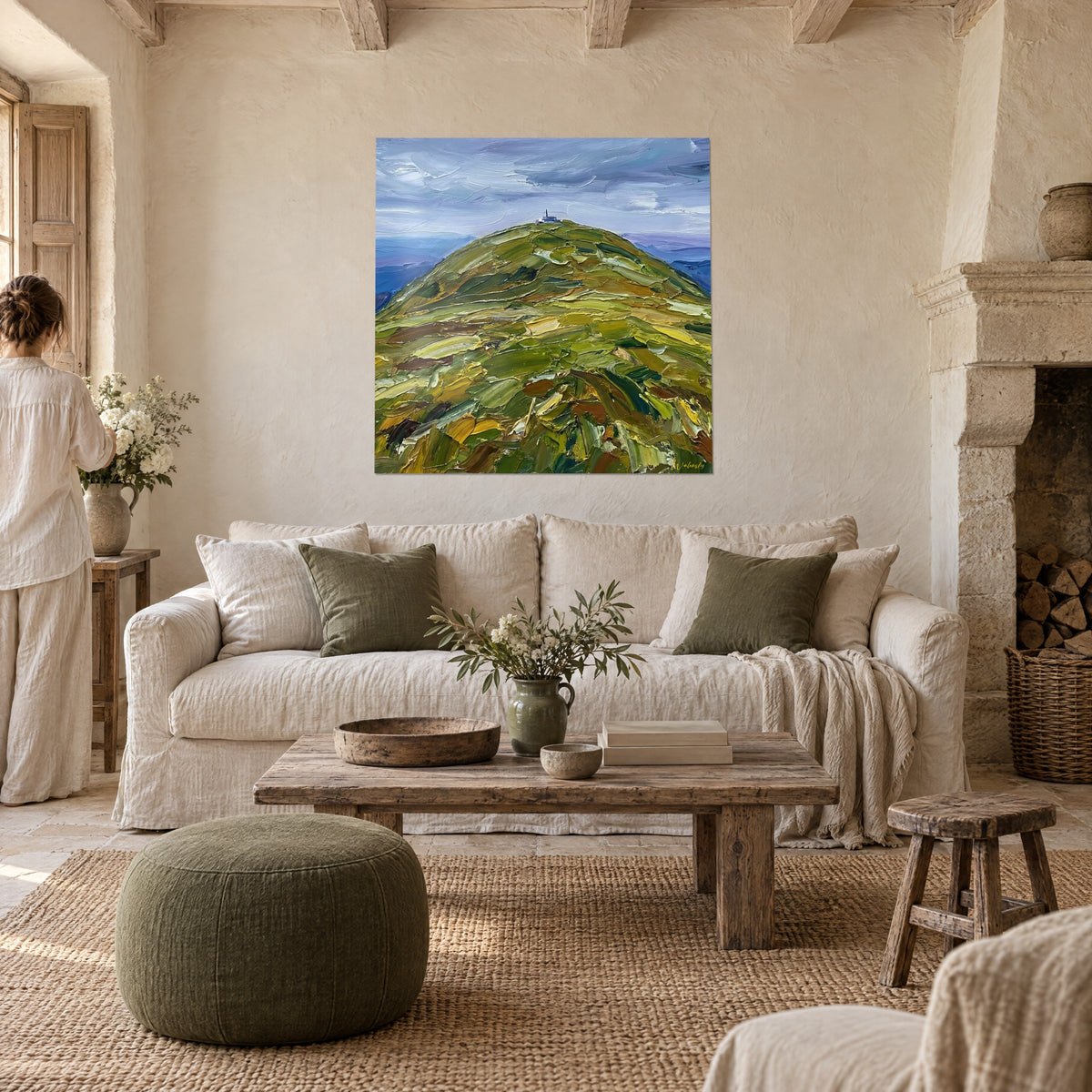 Quadro collina verde dai rilievi ocra e marroni sotto un cielo grigio-azzurro mosso, sopra un divano in un soggiorno luminoso