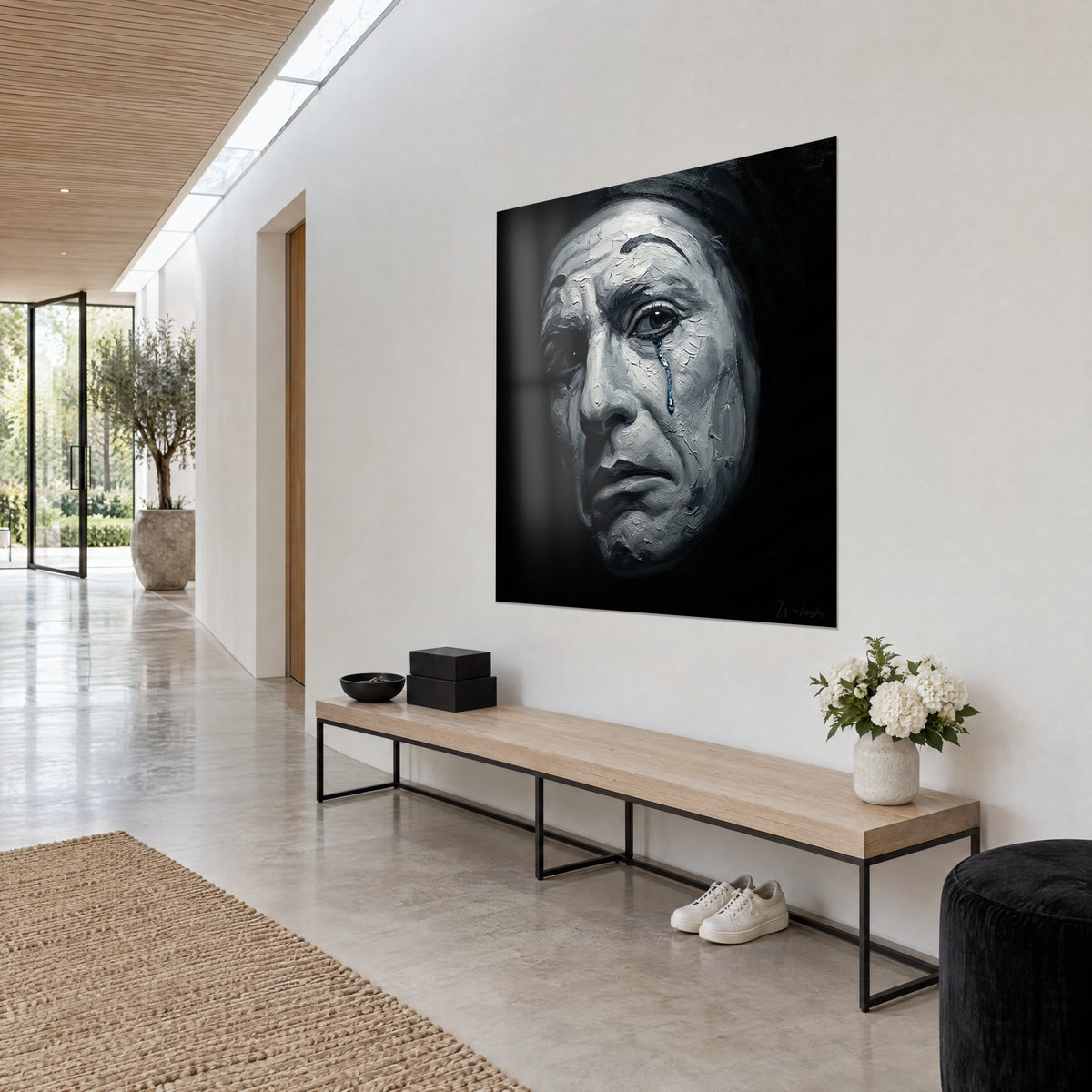 Tableau Pierrot au maquillage blanc craquelé, sourcil noir et larme bleue sur fond sombre, mur clair d'un couloir lumineux