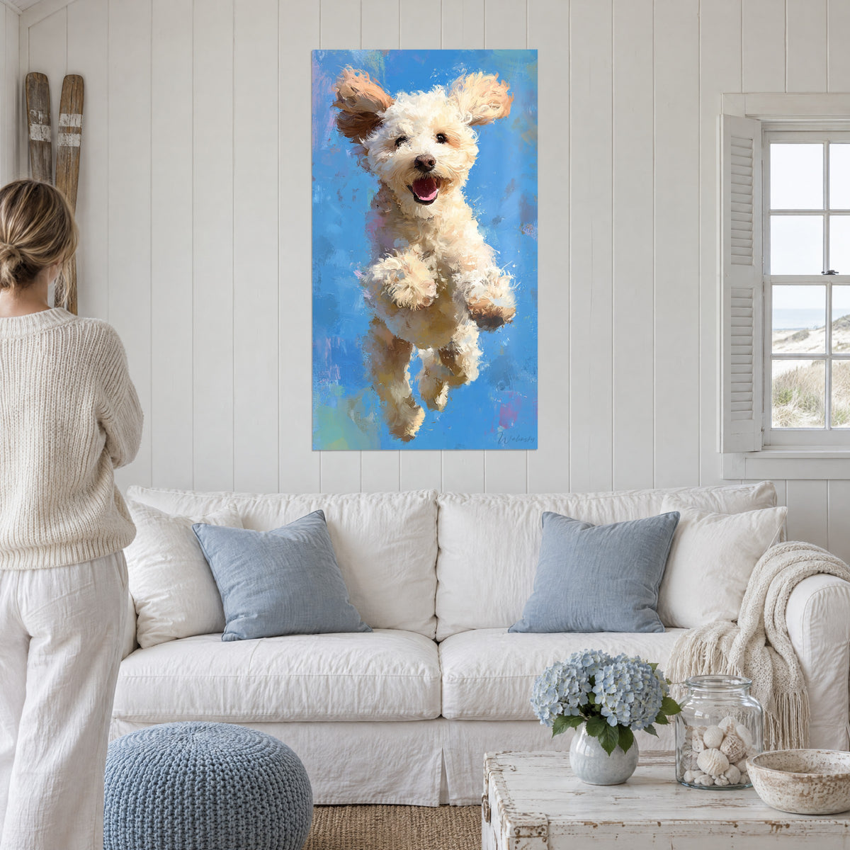 Cuadro caniche color crema saltando sobre fondo azul cielo, orejas al viento, sobre un sofá en un salón luminoso