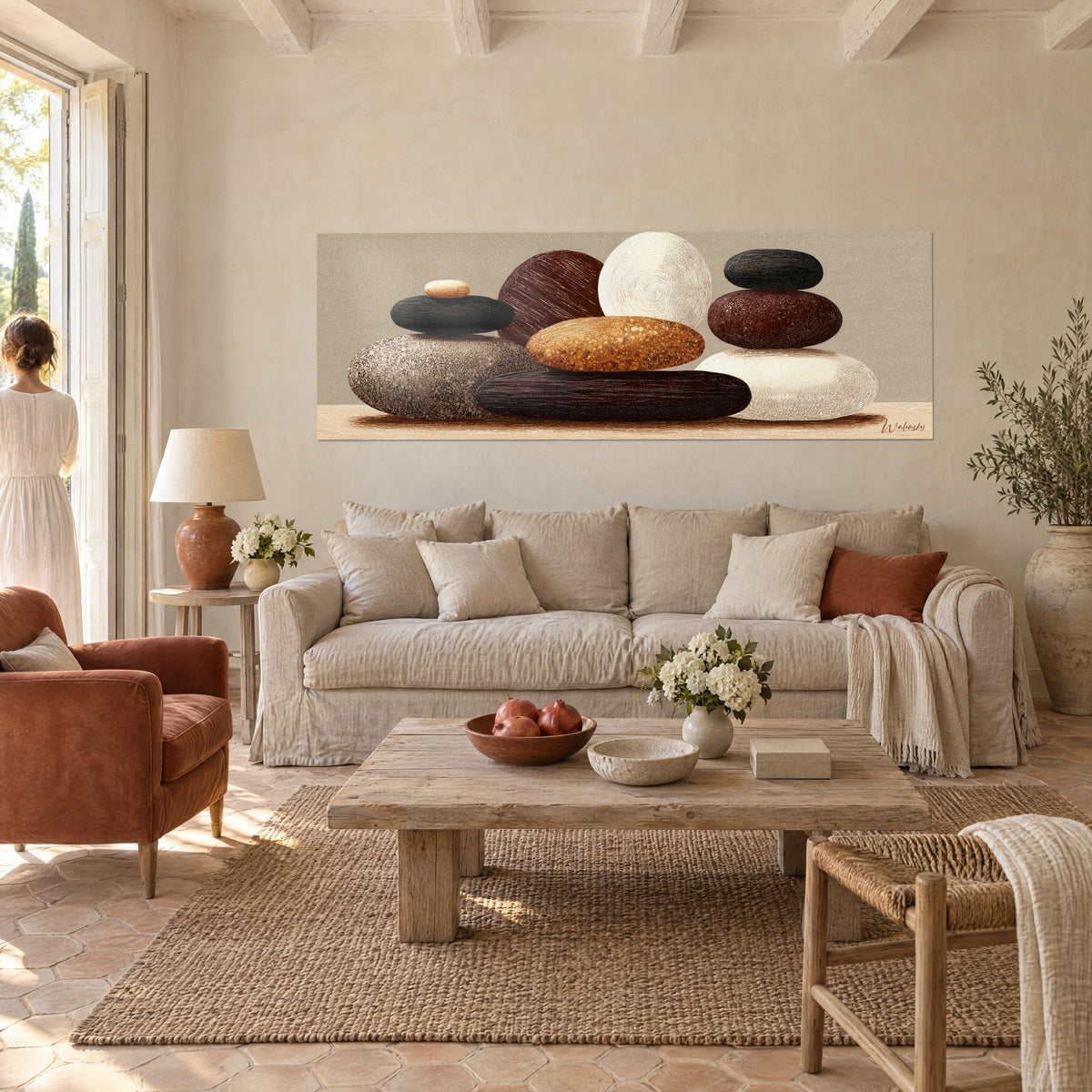 Cuadro guijarros apilados en equilibrio, negro, ocre y blanco crema, dos personas de espaldas, encima de un sofá en un salón luminoso