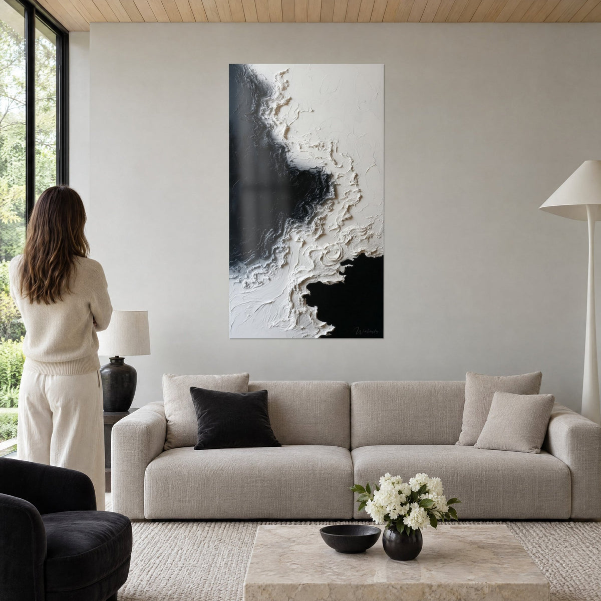 Schilderij abstract met reliëf in antraciet zwart en gebroken wit, vrouw van achteren ervoor, boven een bank in een lichte woonkamer