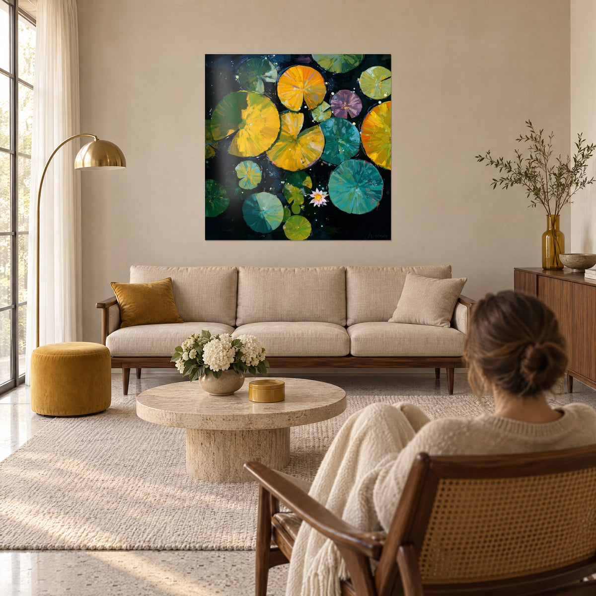 Schilderij van oranje en gele waterlelies van bovenaf gezien, roze bloem in het midden, vrouw van achteren, boven een bank in een lichte woonkamer