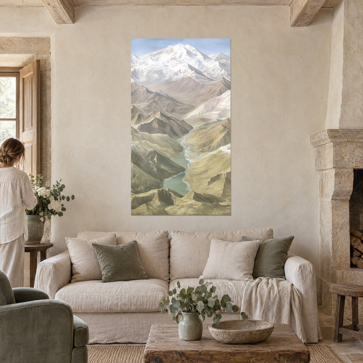 Tableau massif enneigé dominant une vallée glaciaire, rivière turquoise et pentes ocre ; femme de dos, au-dessus d'un canapé dans un salon lumineux