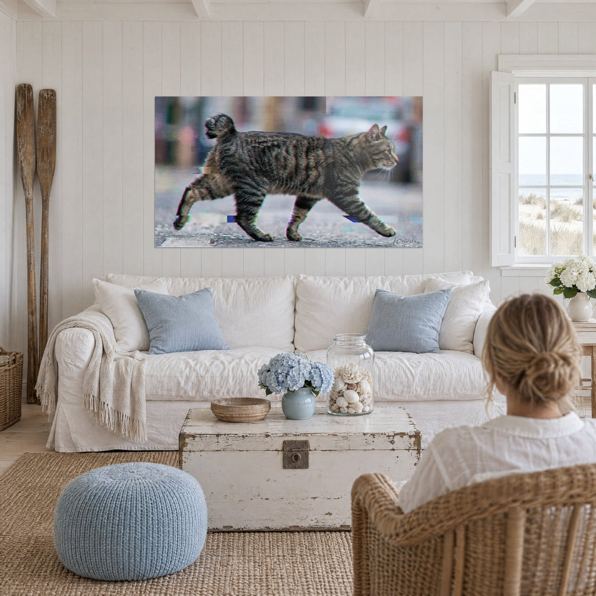 Tableau chat tigré en pleine marche, pelage gris et brun, queue en pompon, au-dessus d'un canapé dans un salon lumineux