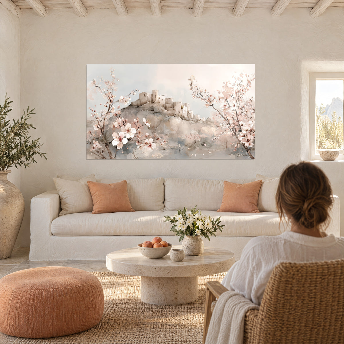 Gemälde Zitadelle aus hellem Stein unter Mandelbäumen, blassrosa Blüten und graublauer Himmel, über einem Sofa in einem hellen Wohnzimmer
