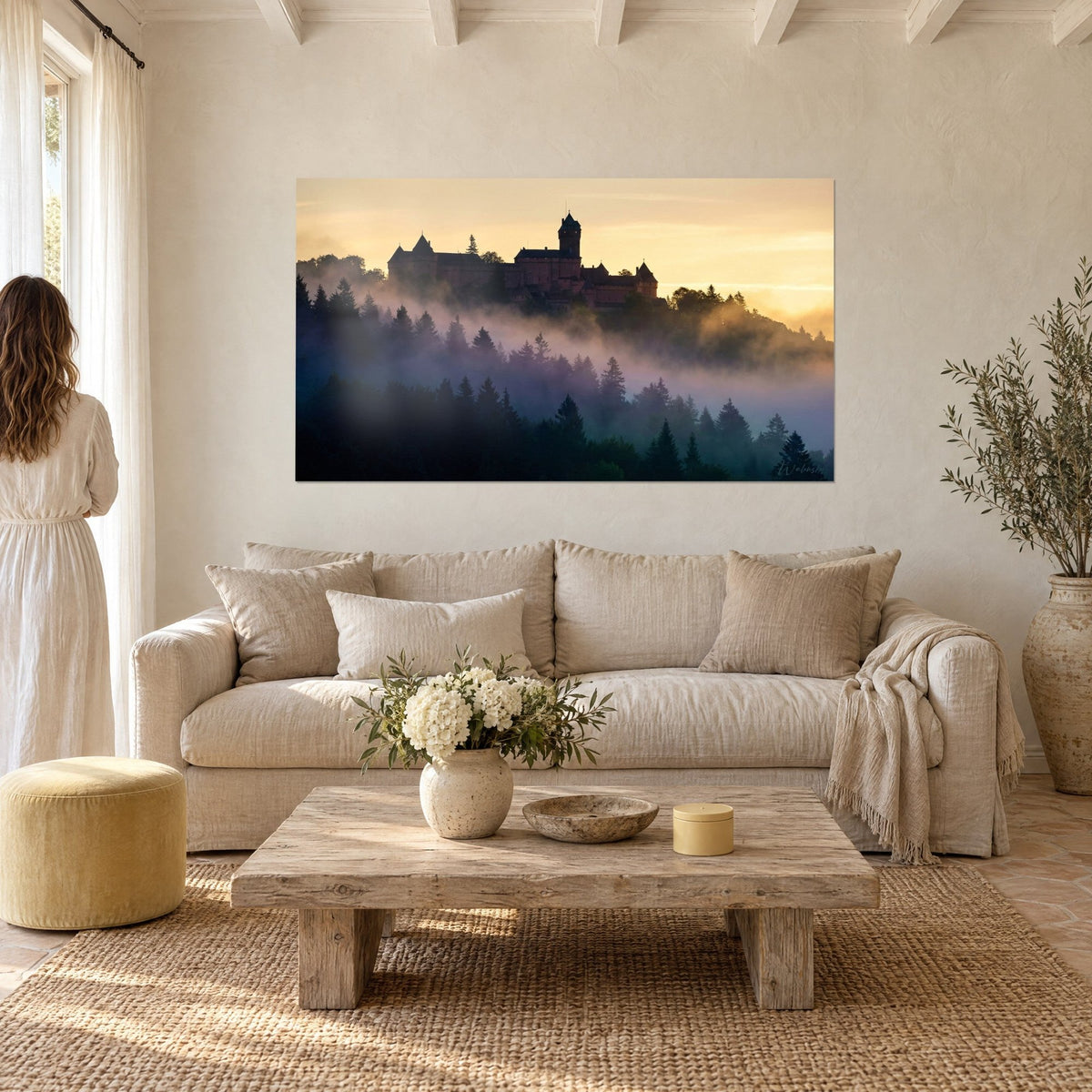 Gemälde Festung aus rosa Sandstein auf einem Bergkamm, violette Nebelschwaden und goldener Himmel, über einem Sofa in einem hellen Wohnzimmer
