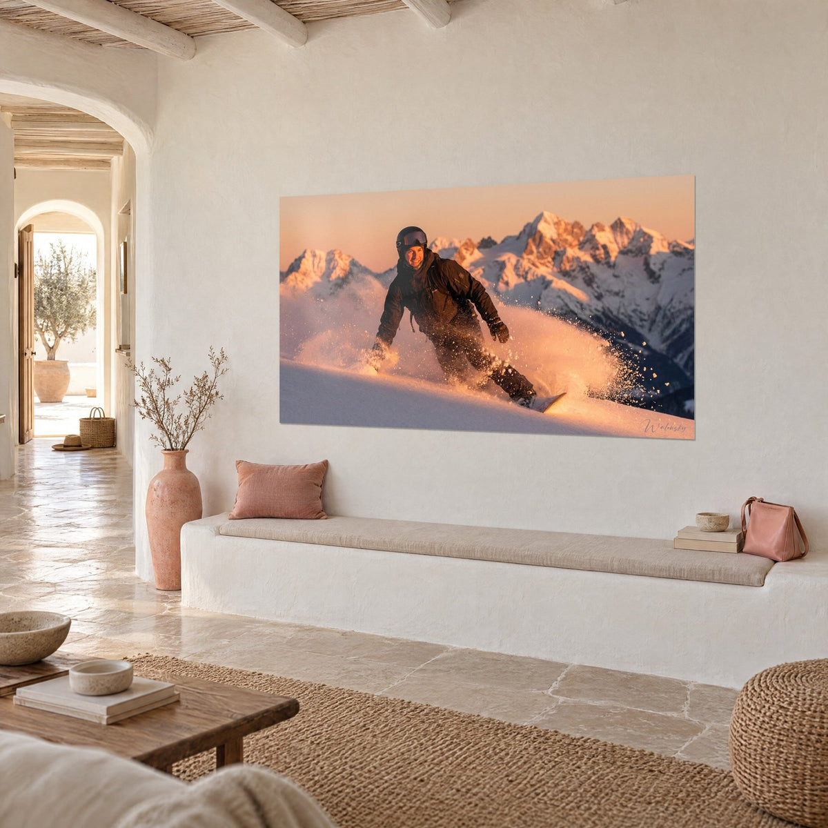 Cuadro de un rider con casco y máscara en una nube de nieve ámbar, cumbres rosadas sobre cielo melocotón, vista de tres cuartos en una pared blanca
