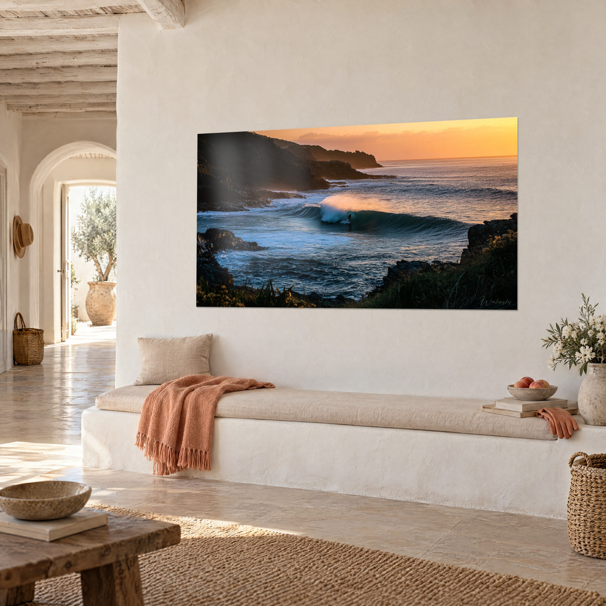 Tableau houle turquoise frangée d'écume blanche sous un ciel abricot et des rochers noirs, banquette claire d'une maison méditerranéenne