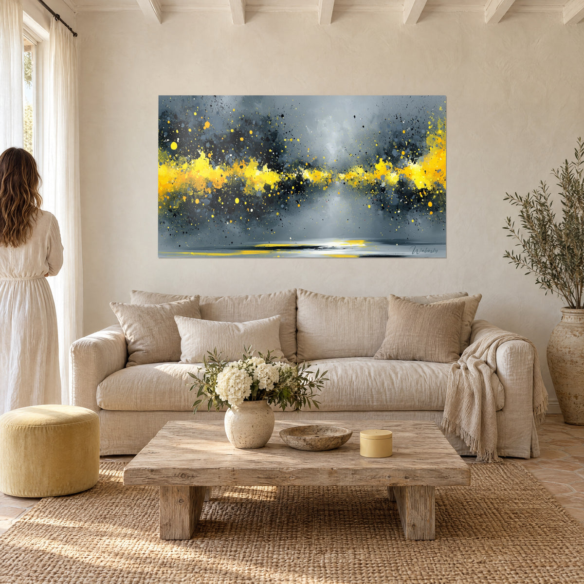Wall art with a cloud of sunny yellow sparks on slate grey background, a woman seen from behind above a sofa in a bright living room