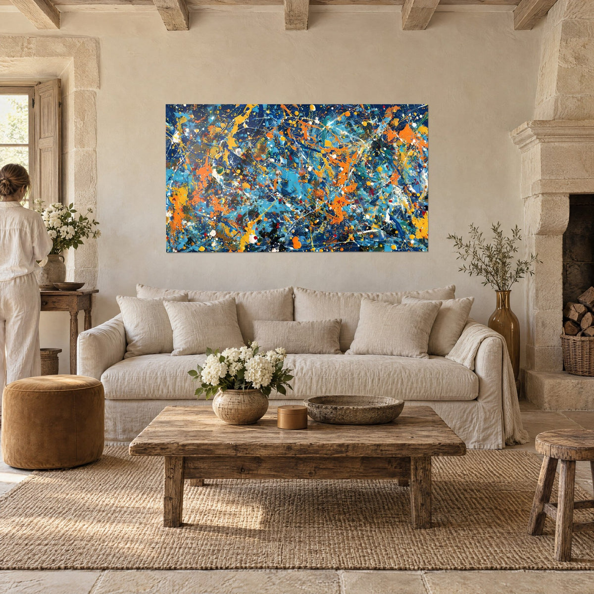Tableau éclaboussures de peinture bleu cobalt et orange vif, une femme de dos, au-dessus d'un canapé dans un salon lumineux