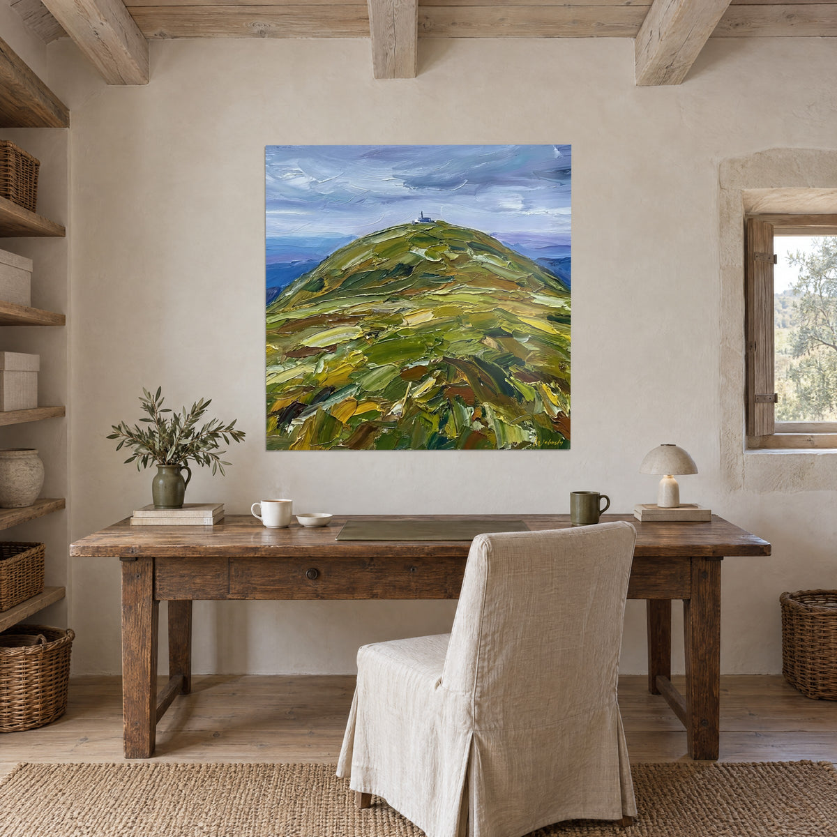 Quadro paesaggio collinare con impasti verdi, marroni e dorati sormontato da una piccola torre, appeso alla parete di uno studio rustico