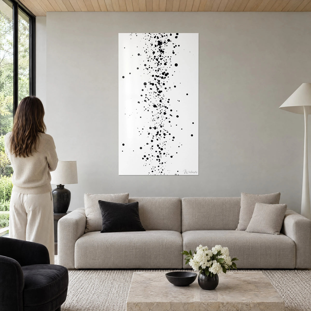 Quadro di gocce d'inchiostro nero in colonna su sfondo bianco, donna di spalle, toni greige e crema, sopra un divano in un soggiorno luminoso
