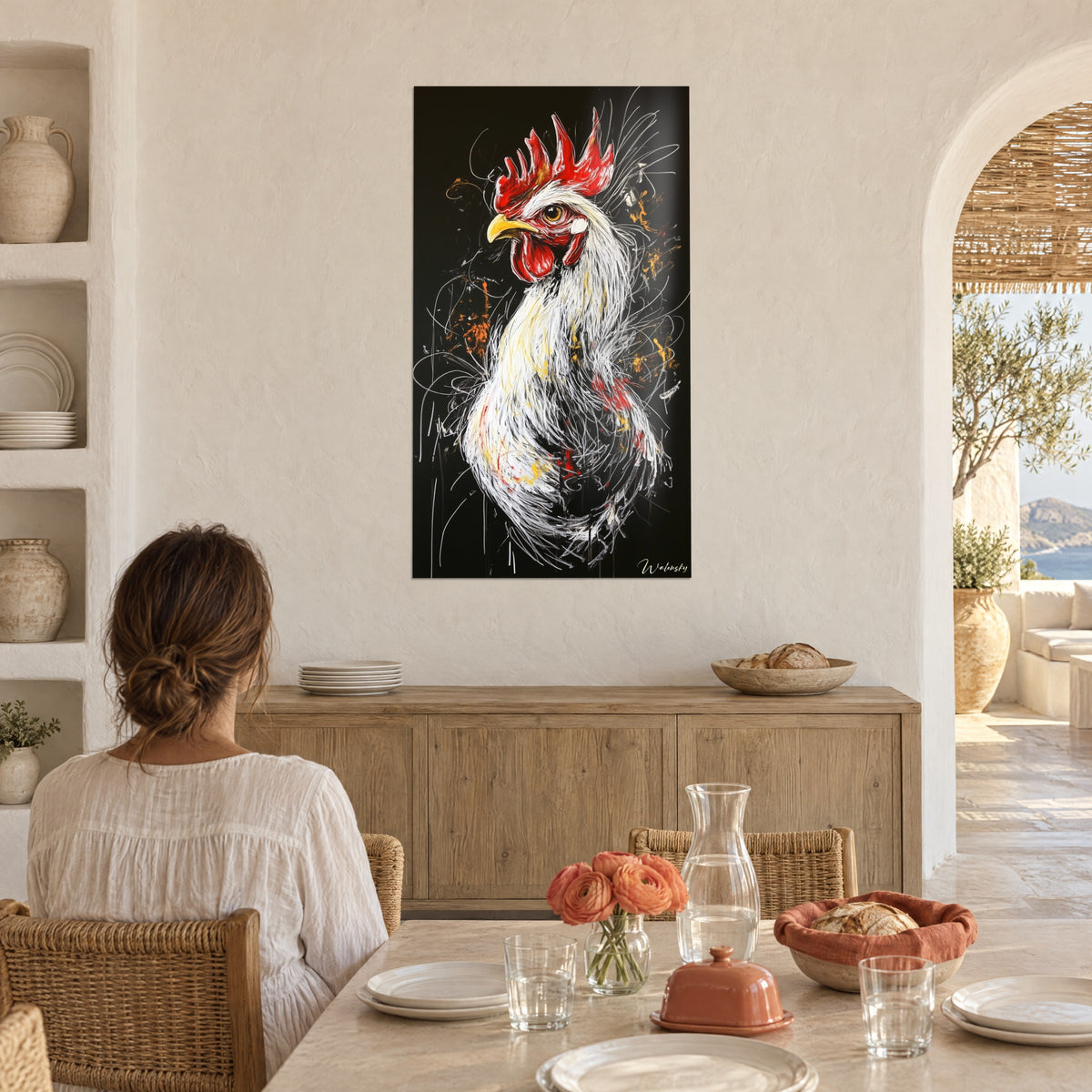 Πίνακας με πτηνό με ατημέλητα λευκά φτερά, κεχριμπαρένιο μάτι και κόκκινα λοβάρια, απέναντι από γυναίκα καθισμένη σε τραπέζι σε μεσογειακή κουζίνα