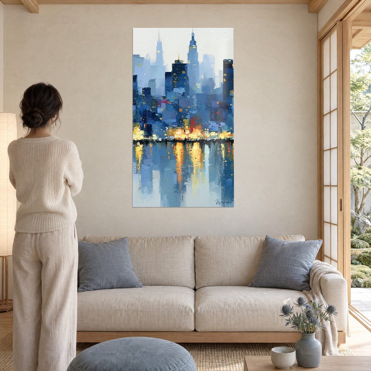 Tableau gratte-ciel givrés bleu cobalt et reflets dorés sur l'eau, femme de dos, au-dessus d'un canapé dans un salon lumineux