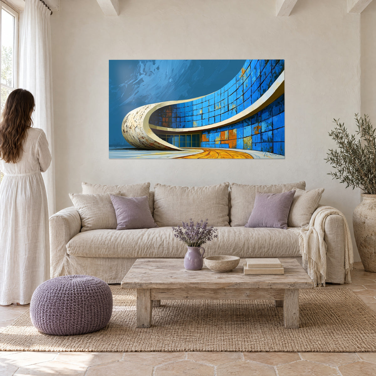 Tableau bâtiment courbe aux carreaux bleu cobalt et taches ocre, contemplé par une femme de dos au-dessus d'un canapé dans un salon lumineux