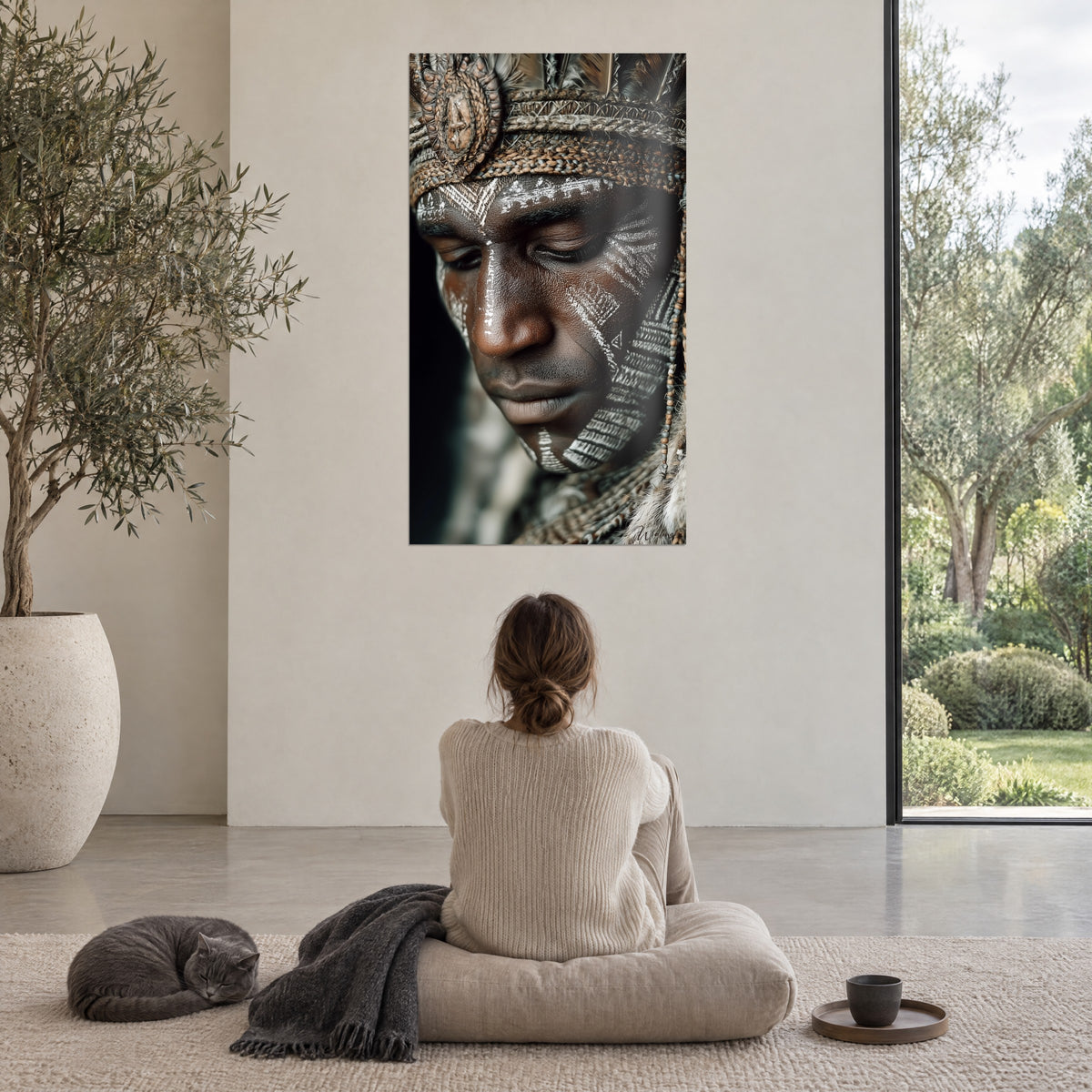 Wall art of a meditative tribal figure, white chevron on brown cheek, grey feathers, facing a grey cushion where a cat sleeps