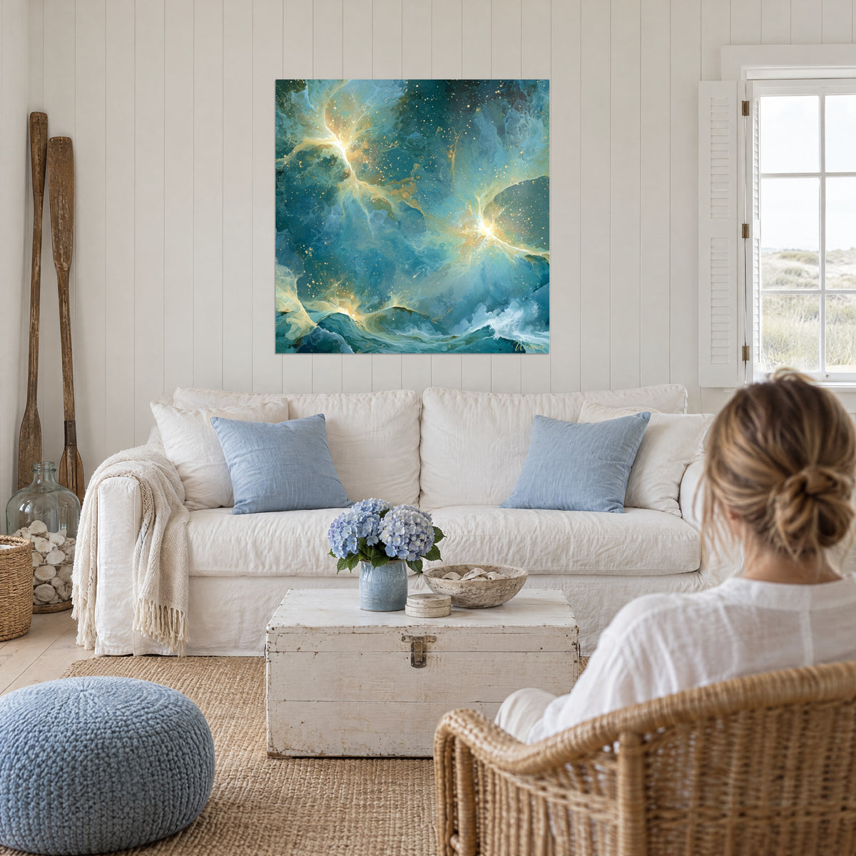 Tableau nébuleuse turquoise et dorée aux éclats lumineux, femme de dos, au-dessus d'un canapé dans un salon lumineux
