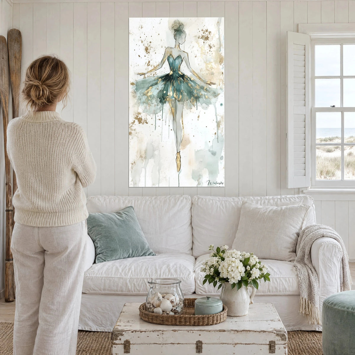 Wall art ballerina in a grey-green tutu flecked with gold glitter, silhouette en pointe, with two people seen from behind, above a sofa in a bright living room