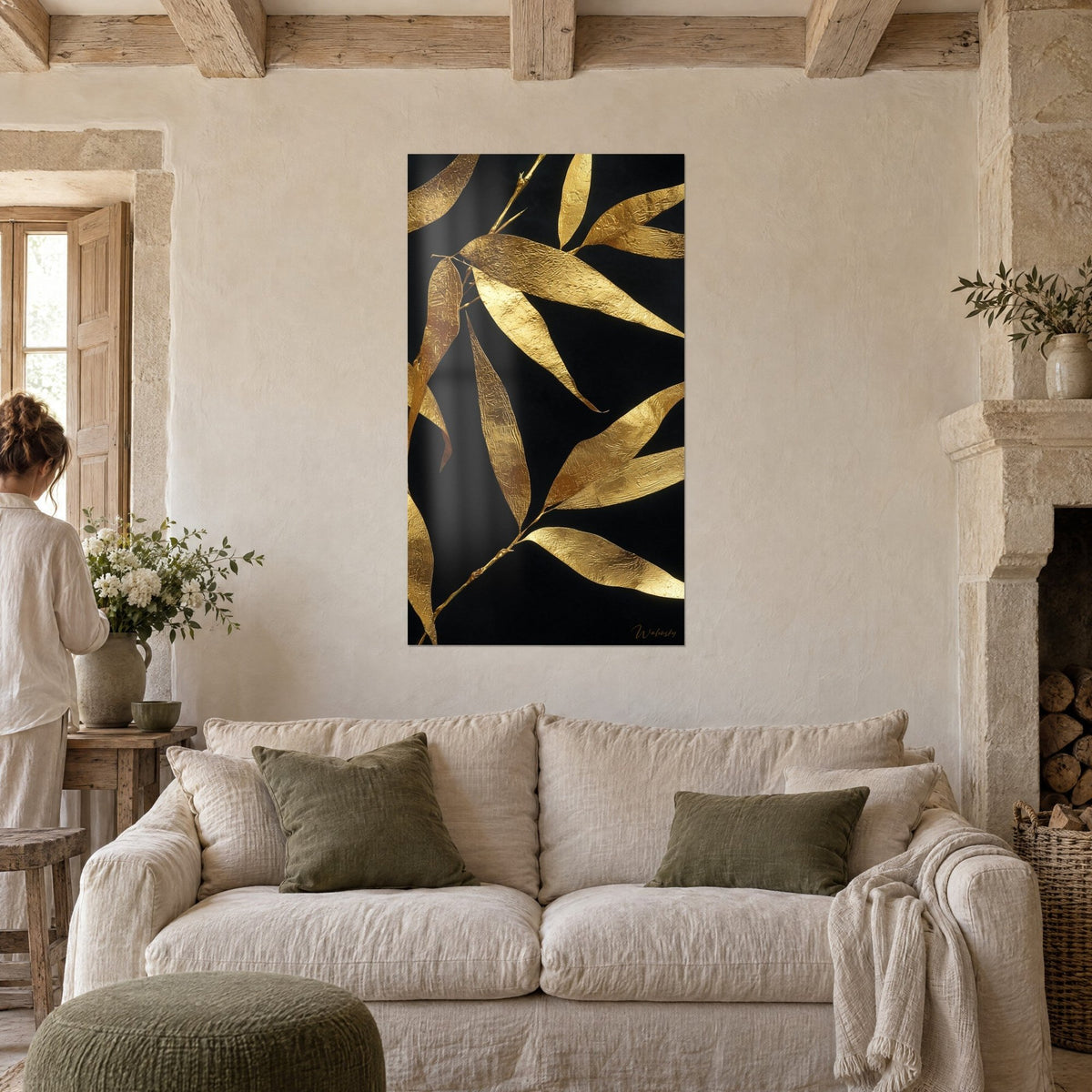 Tableau feuilles de bambou en or martelé sur fond noir profond, jeune femme de dos, au-dessus d'un canapé dans un salon lumineux