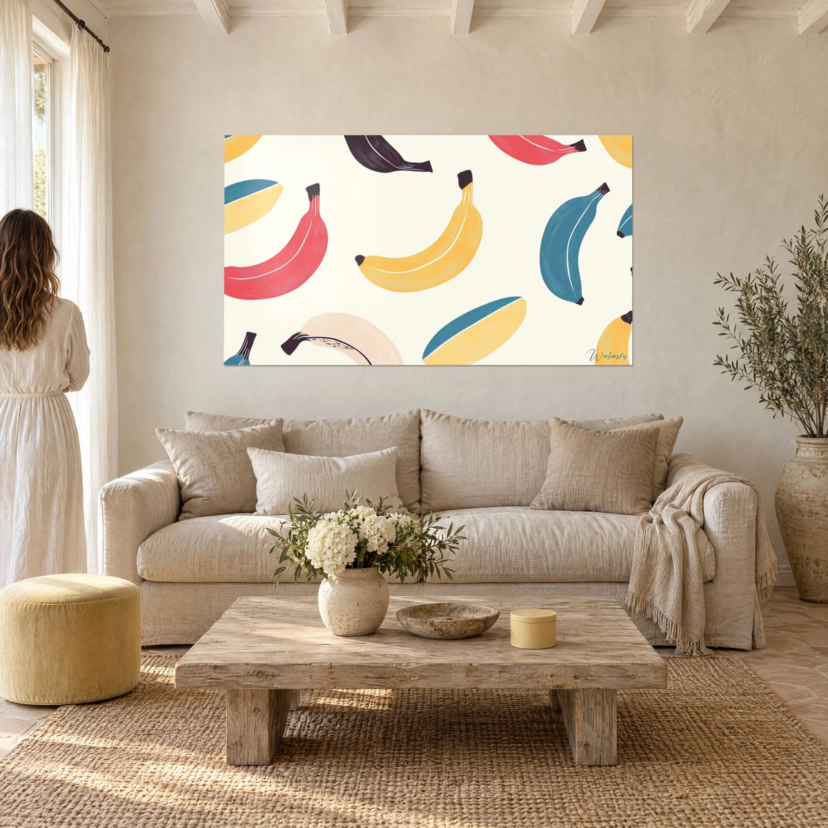 Cuadro de plátanos en linograbado amarillo azafrán y rosa coral sobre fondo crema, encima de un sofá en un salón luminoso