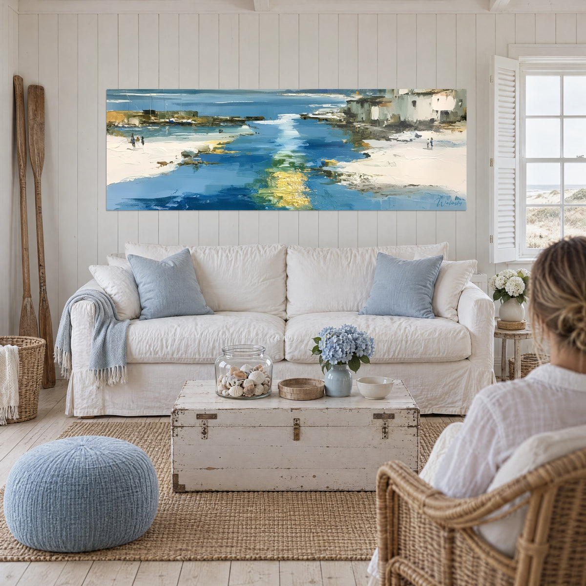 Gemälde Hafen mit goldgestreiften blauen Wassern, weiße Fassaden und Silhouetten am Strand, über einem Sofa in einem hellen Wohnzimmer