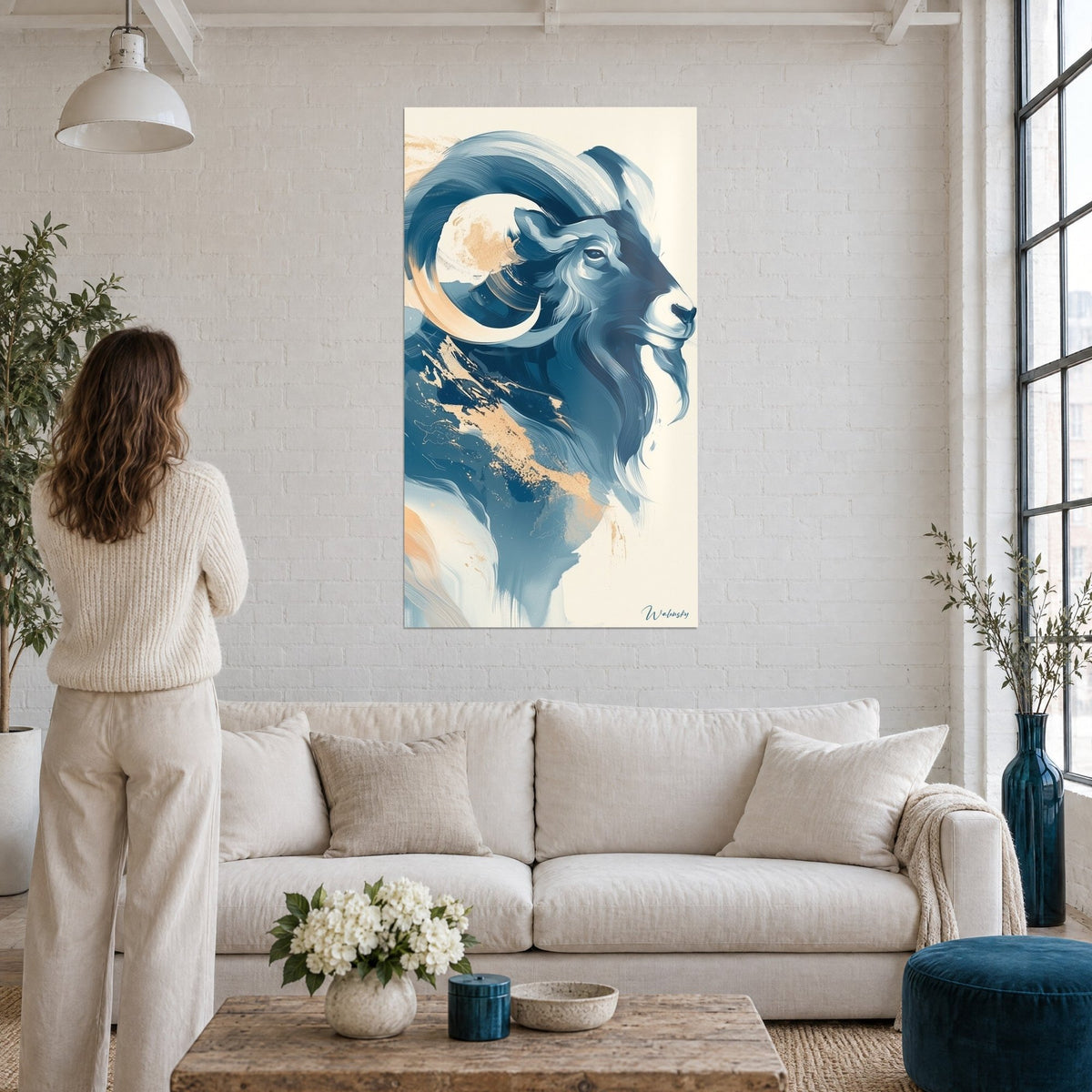 Quadro ariete stilizzato con corna a spirale blu notte e pesca, una donna di spalle, sopra un divano in un soggiorno luminoso