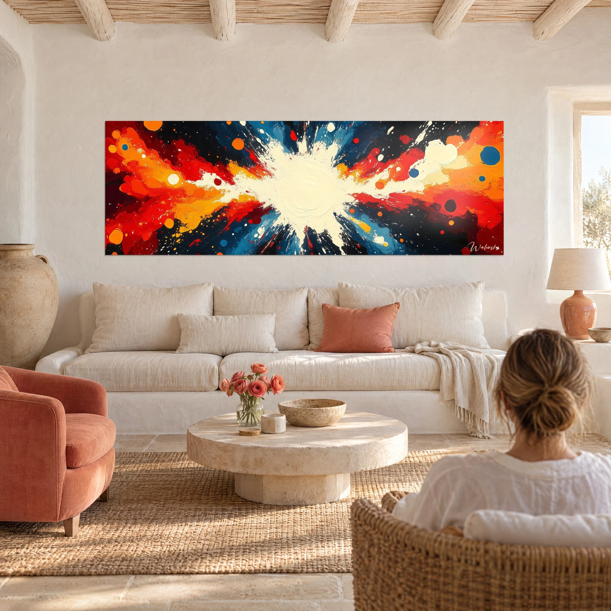 Cuadro explosión de pintura en rojo, naranja y azul alrededor de un núcleo crema, sobre un sofá en un salón luminoso