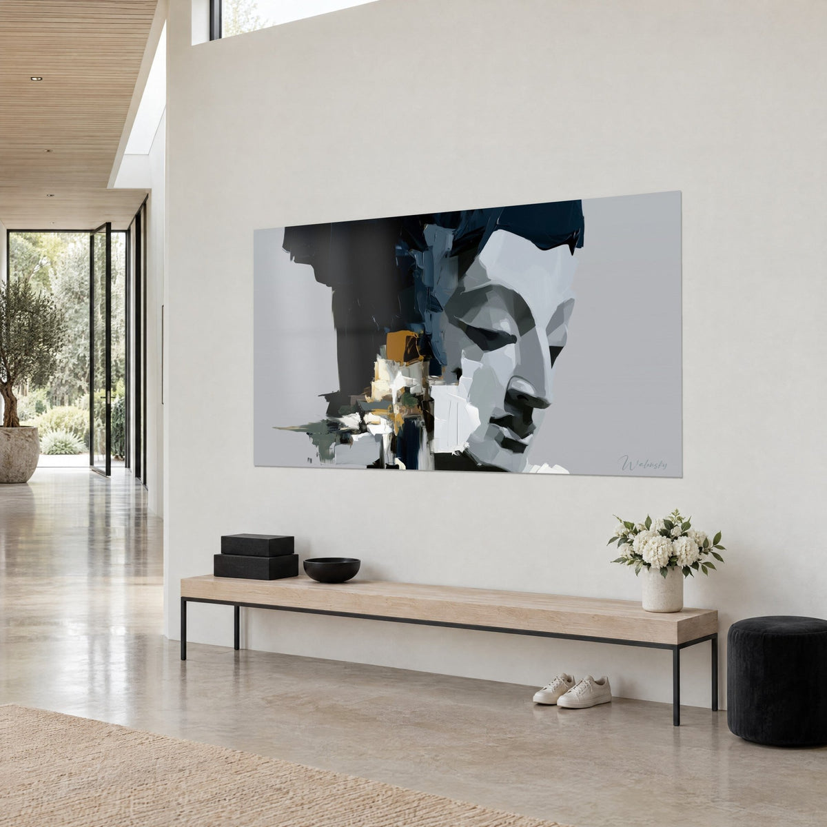 Tableau visage sculpté en blocs blanc et gris, coulures noires et touches ocre sur fond gris clair, au-dessus d'un banc dans un séjour