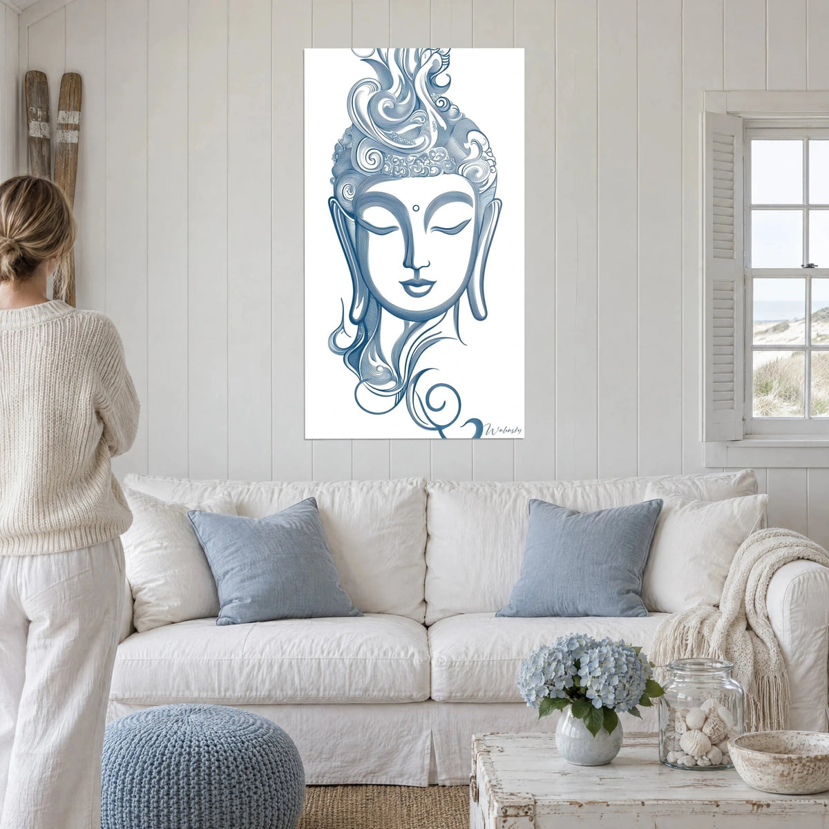 Tableau visage de Bouddha aux yeux clos, traits bleu acier sur blanc, volutes de chevelure, au-dessus d'un canapé dans un salon lumineux