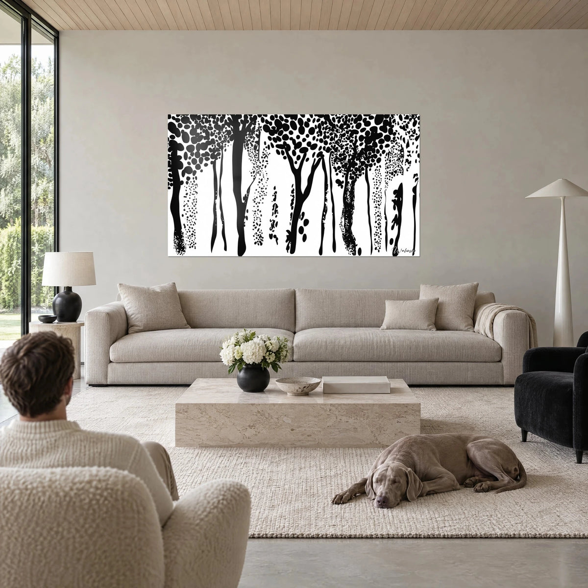 Tableau forêt stylisée de troncs noirs sur fond blanc, feuillage en taches ovales, au-dessus d'un canapé dans un salon lumineux