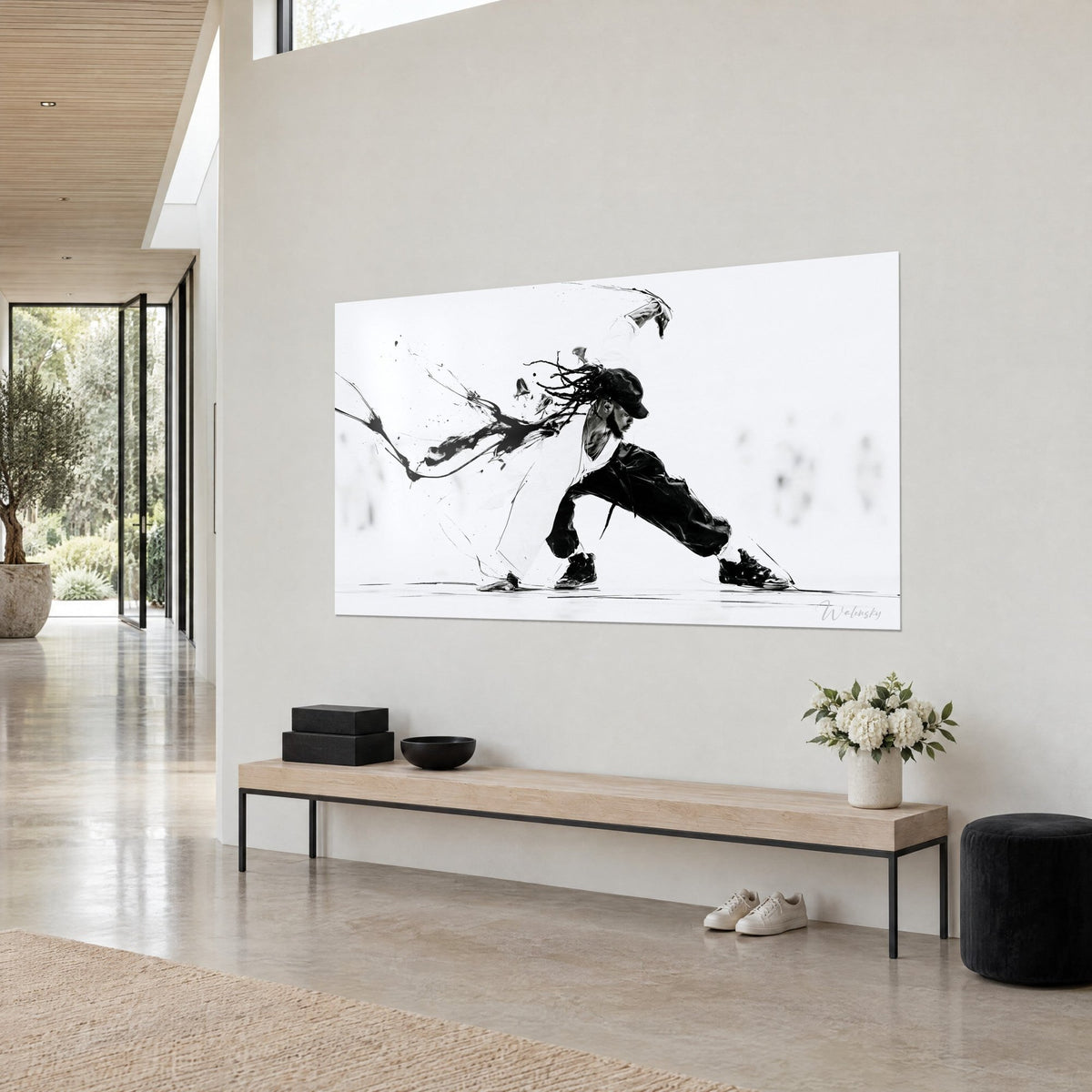 Wall art of a crouching b-boy in a split, black ink splashes on a white background, seen from three-quarter view above a wooden bench in a lounge