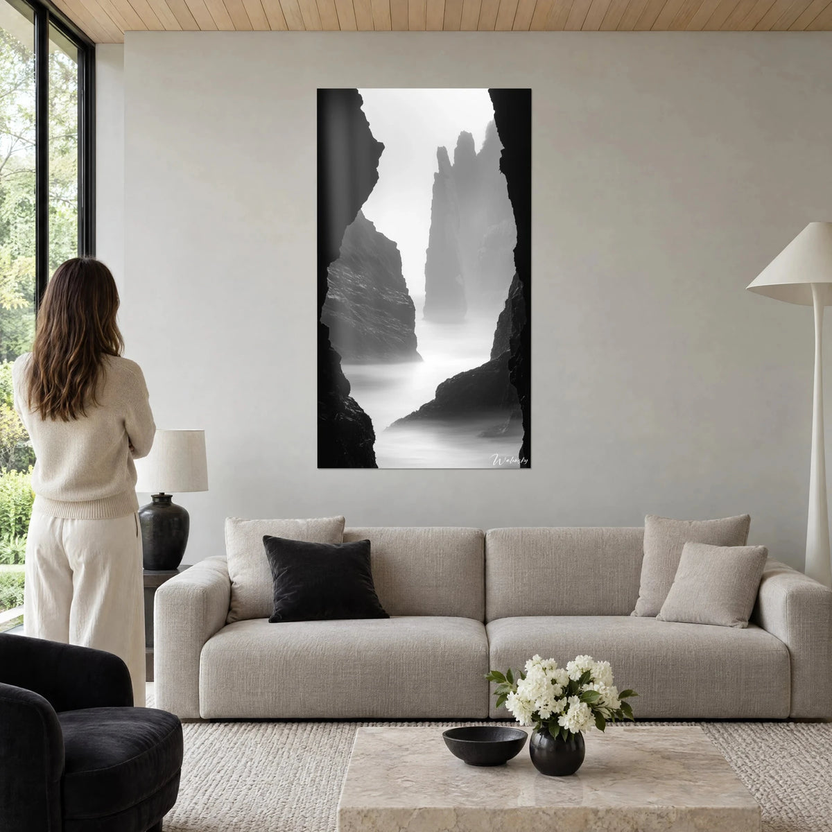 Gemälde Klippen im Nebel, perlgraue Felsnadel zwischen zwei schwarzen Wänden, Frau von hinten, über einem Sofa in einem hellen Wohnzimmer
