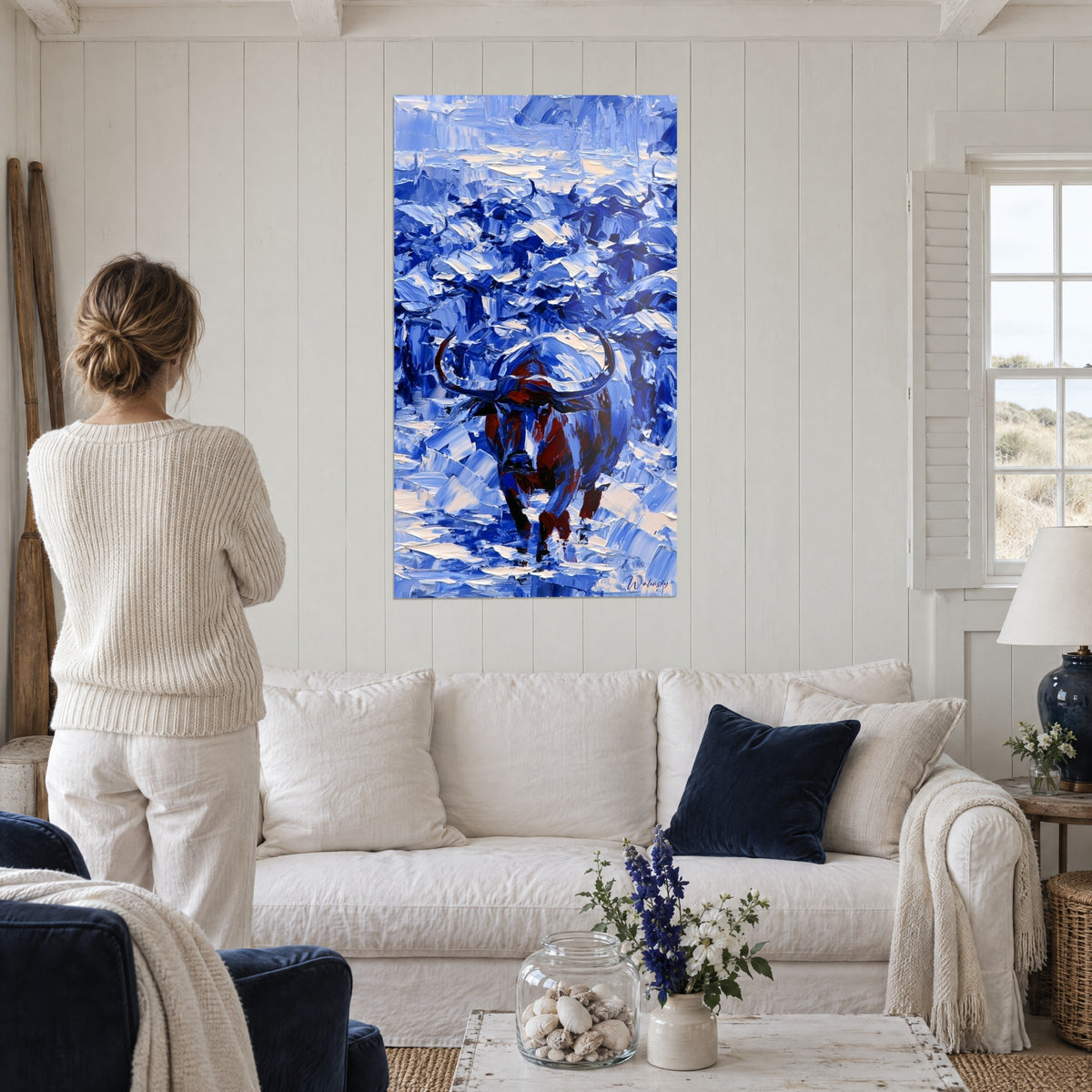 Cuadro búfalo macizo de cuernos curvados, pelaje rojizo sobre trazos de espátula azules y crema, encima de un sofá en un salón luminoso