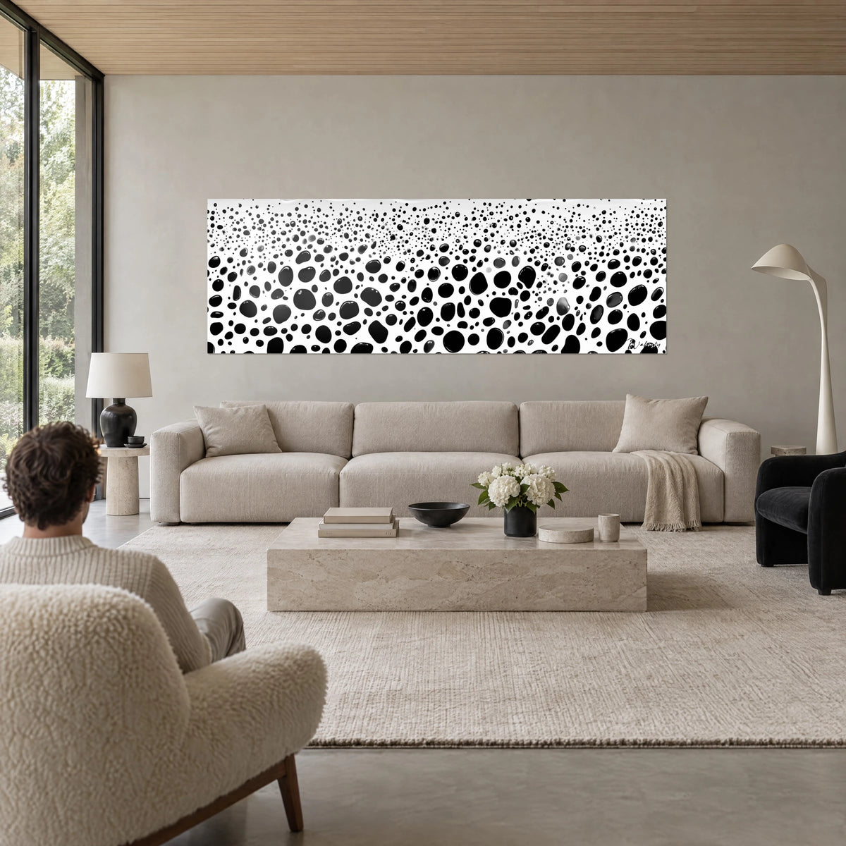 Cuadro con gotas de tinta negra sobre fondo blanco, burbujas de tamaños variados, una persona de espaldas, encima de un sofá en un salón luminoso