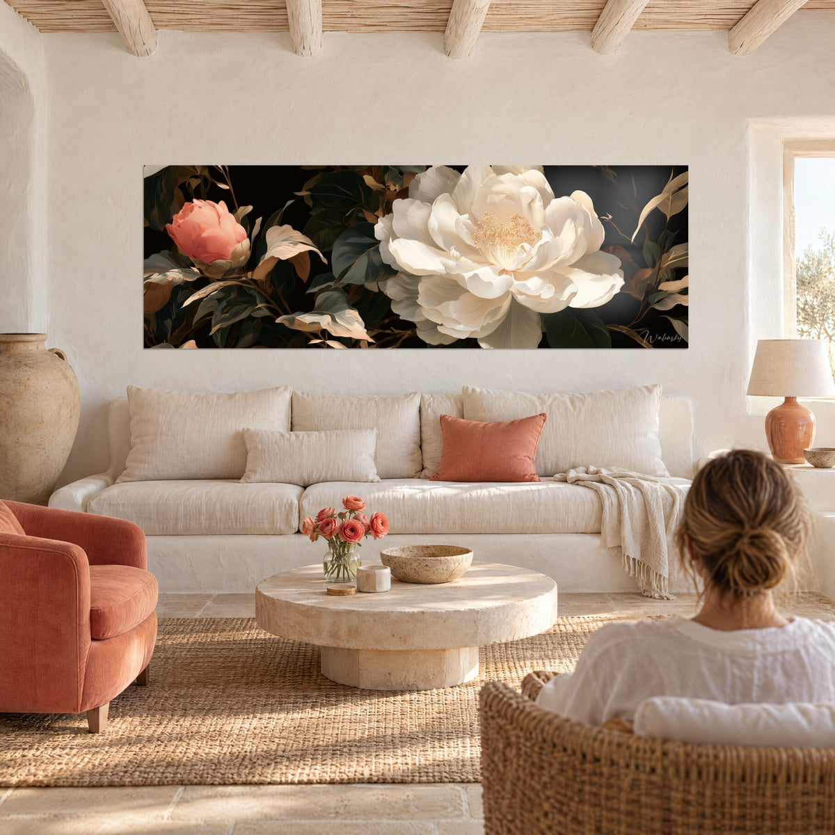 Wall art of an ivory camellia in full bloom beside a coral pink bud, dark golden foliage, woman seen from behind, above a sofa in a bright living room