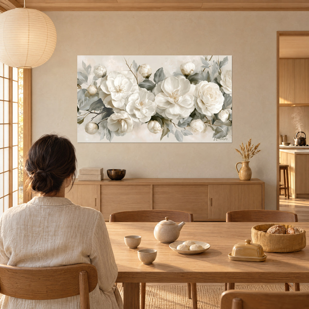 Quadro di fila di rose bianche sbocciate, boccioli avorio e fogliame grigio salvia, donna di spalle a un tavolo di legno, sala da pranzo japandi