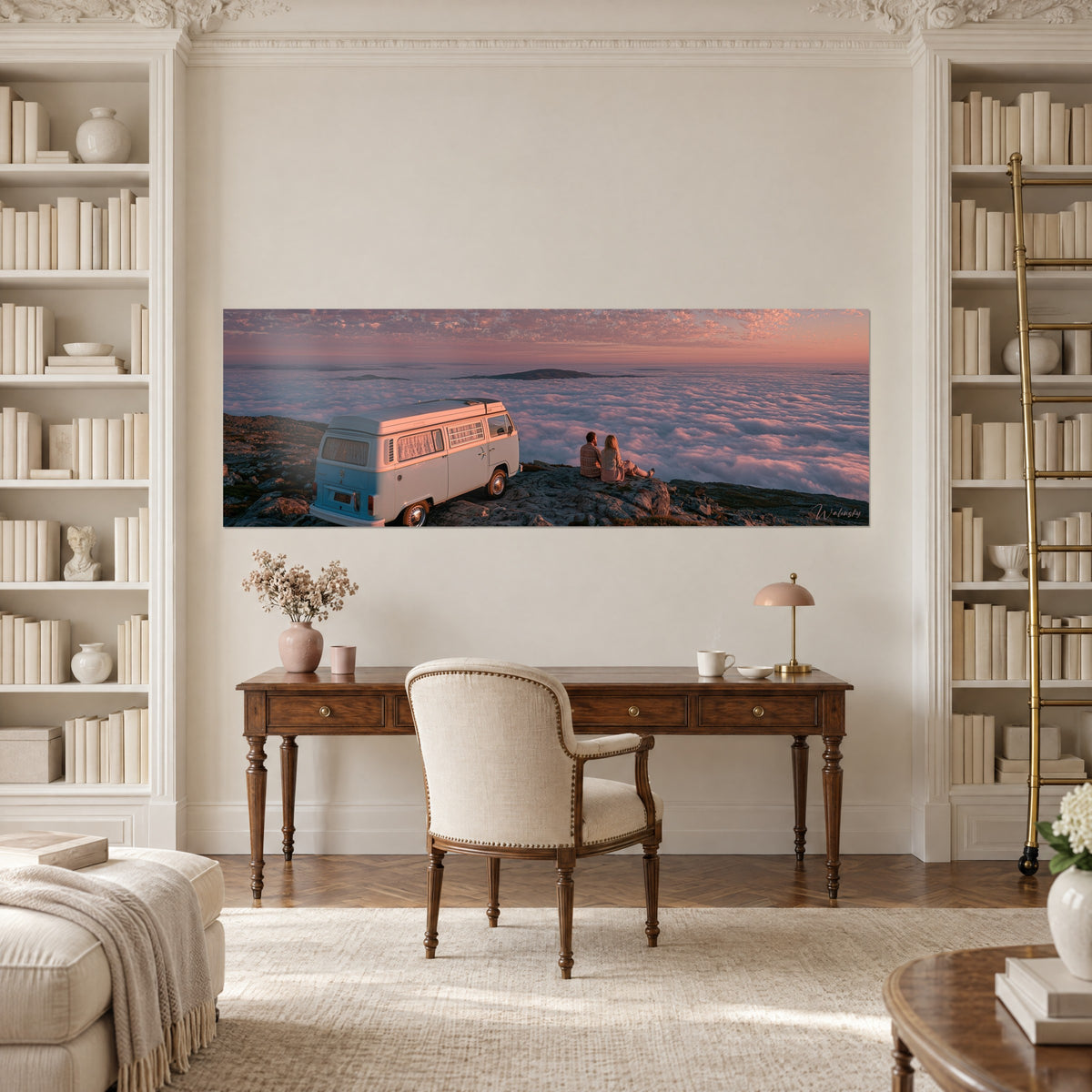 Schilderij van een turquoise en witte vintage bestelwagen op een rotsuitsteeksel, roze waas aan de horizon, boven een houten bureau in een kamer met boekenkasten