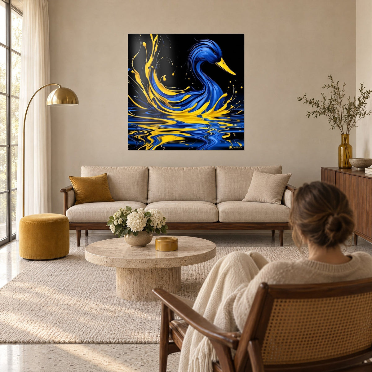Tableau canard indigo au bec jaune soleil, fond noir et éclaboussures dorées, vu par une femme de dos au-dessus d'un canapé dans un salon lumineux