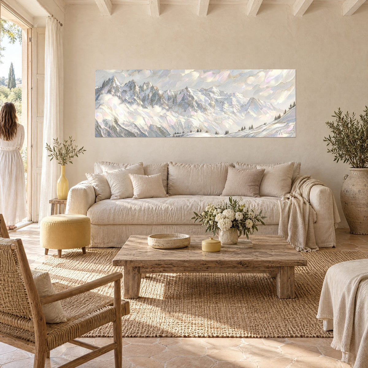Wall art of a massive snow-covered alpine mountain, grey peaks and rosy mother-of-pearl clouds, woman seen from behind, above a sofa in a bright living room