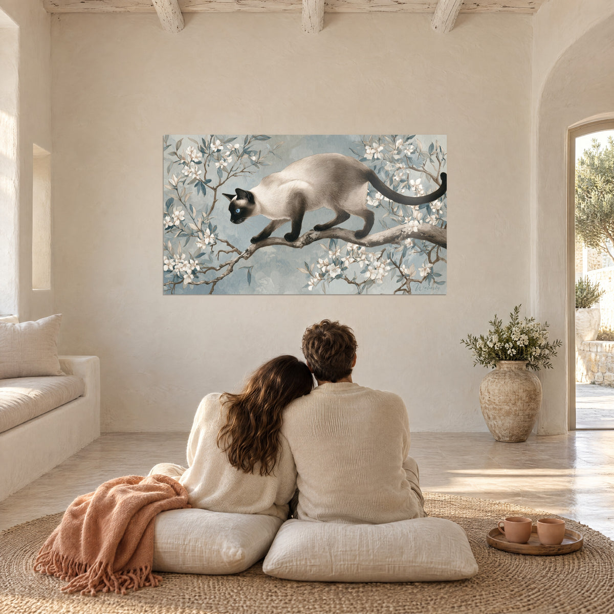 Cuadro gato esbelto de mirada azul, rama nudosa y pétalos marfil sobre fondo azulado, frente a una pareja de espaldas sobre cojines crema