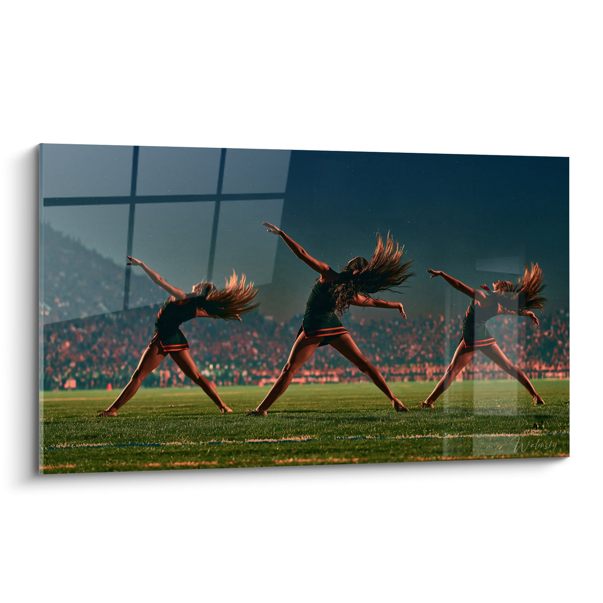 Trois pom-pom girls en vert et orangé, cheveux en mouvement, devant un stade bleu nuit