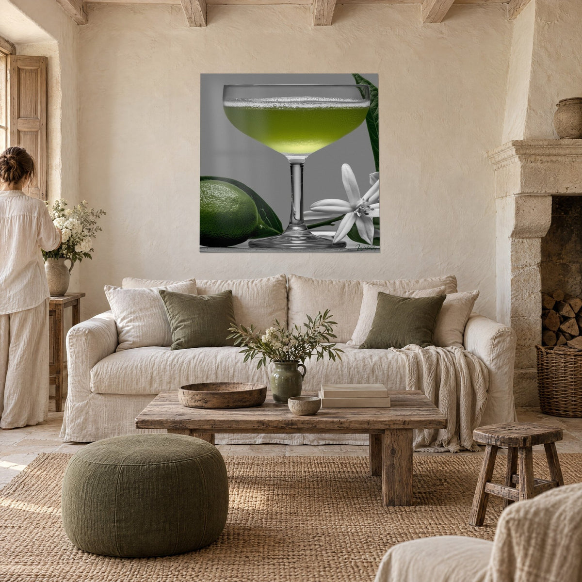 Tableau coupe à cocktail verte et mousse blanche, citron vert et fleur étoilée sur fond gris, au-dessus d'un canapé dans un salon lumineux
