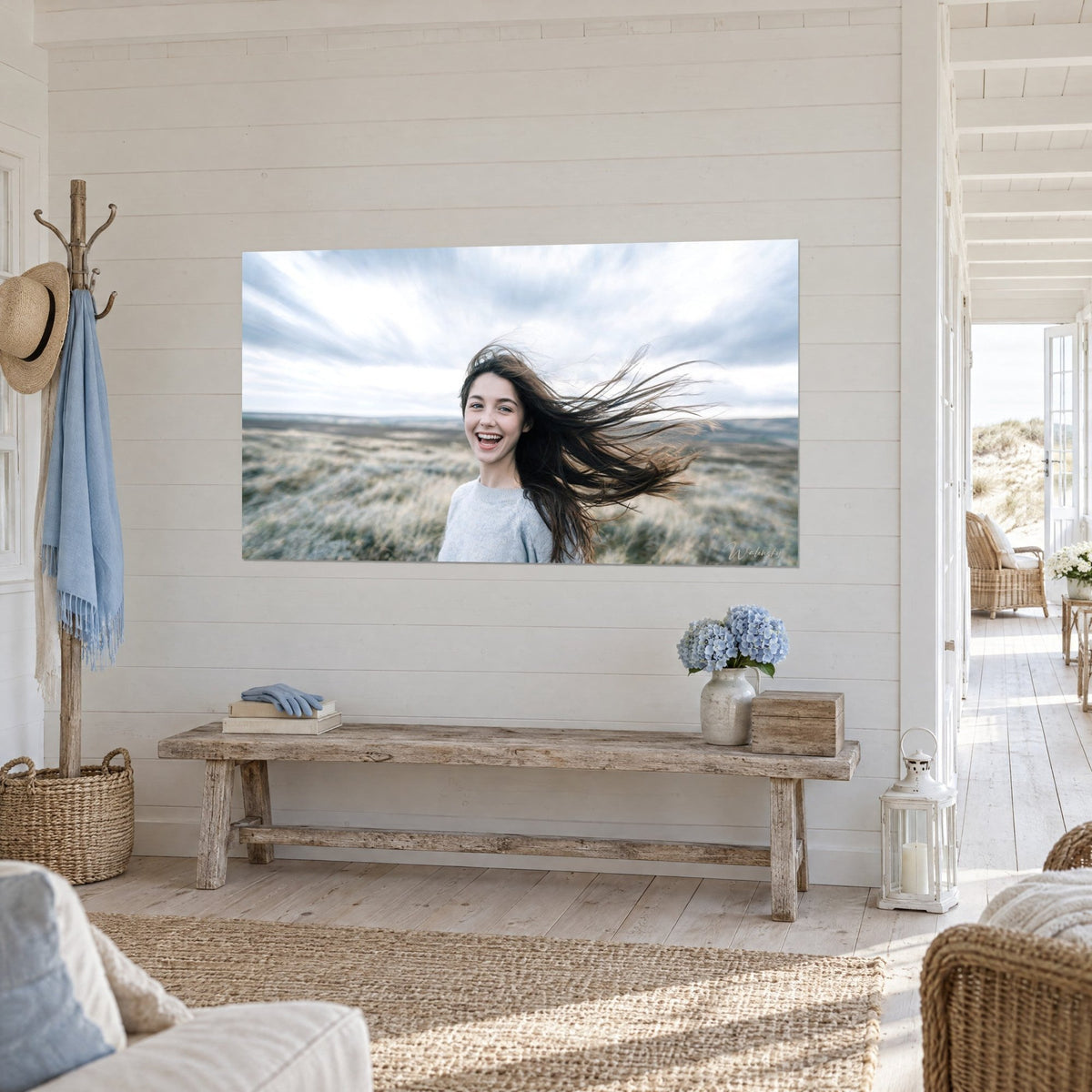 Wall art of a radiant laughing portrait, brown strands blown across a moor of golden grasses and a white sky, three-quarter view, white panelled wall