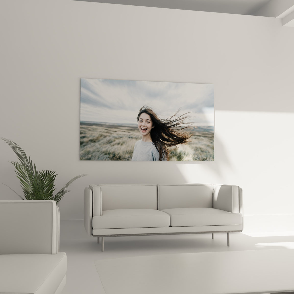 Visage rieur encadré de cheveux bruns, tons beiges et gris, au-dessus d'un canapé dans un salon lumineux