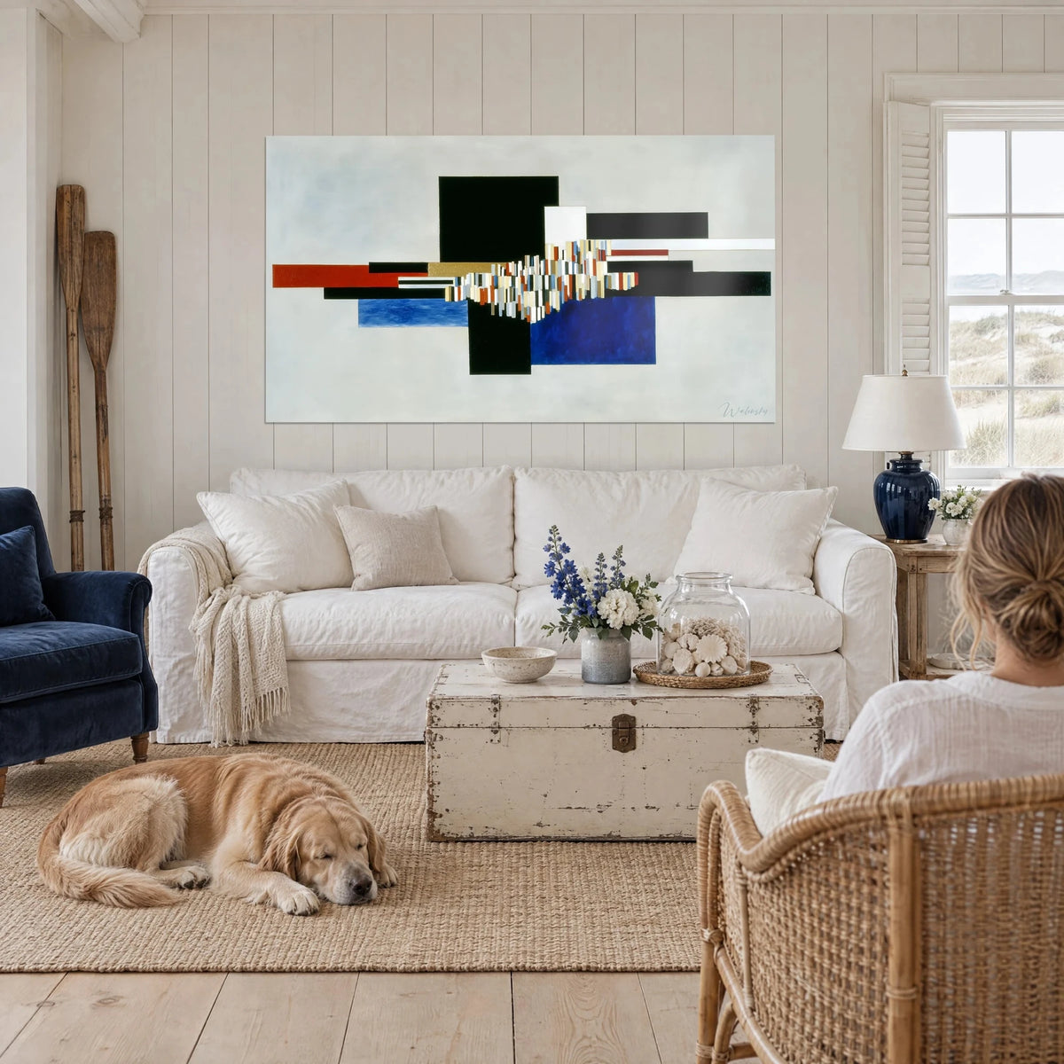 Tableau composition suprématiste de rectangles noirs, rouge brique et bleu cobalt sur fond gris perle, au-dessus d'un canapé dans un salon lumineux