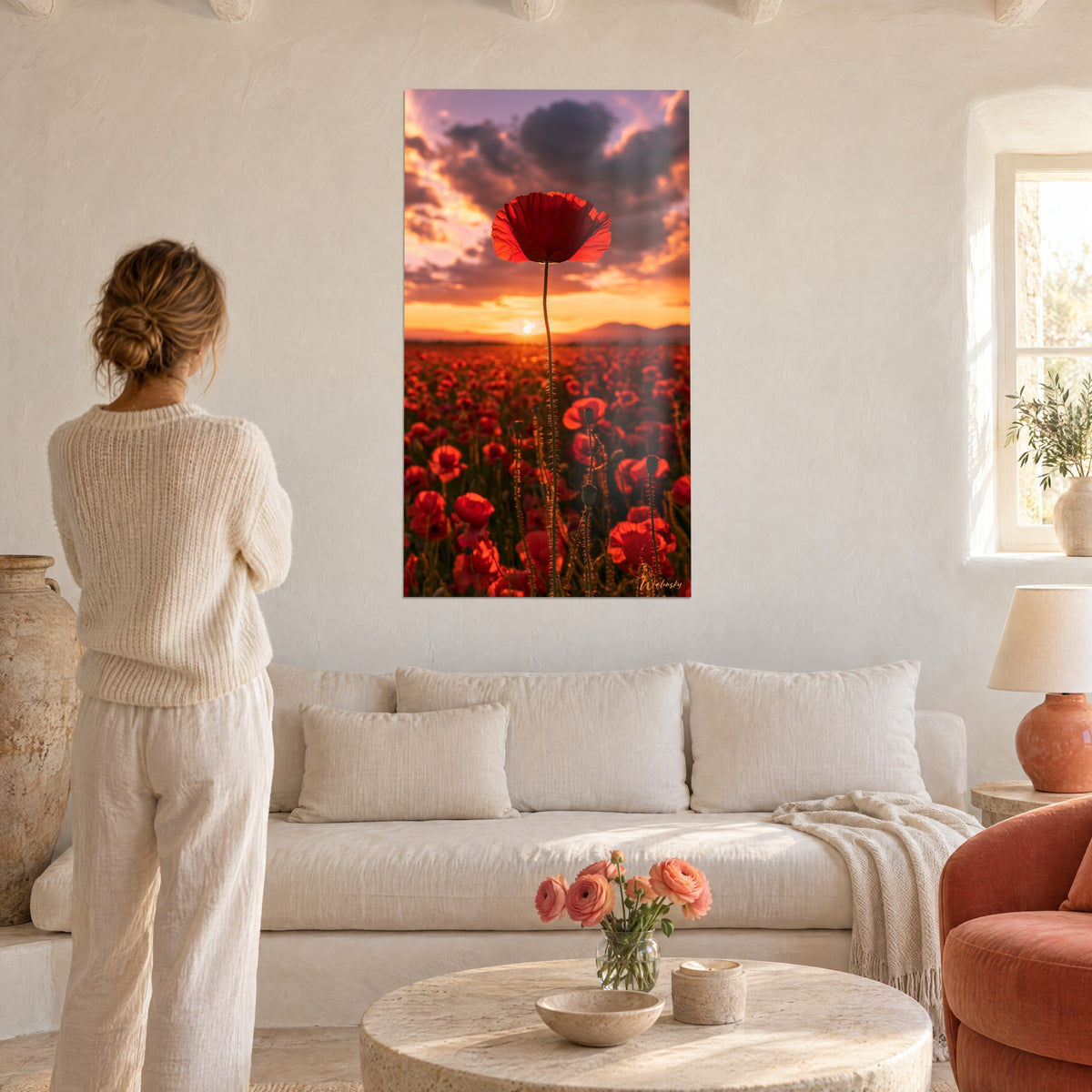 Quadro papavero rosso solitario di rosso vivo su cielo arancio e viola, donna di spalle, sopra un divano in un soggiorno luminoso