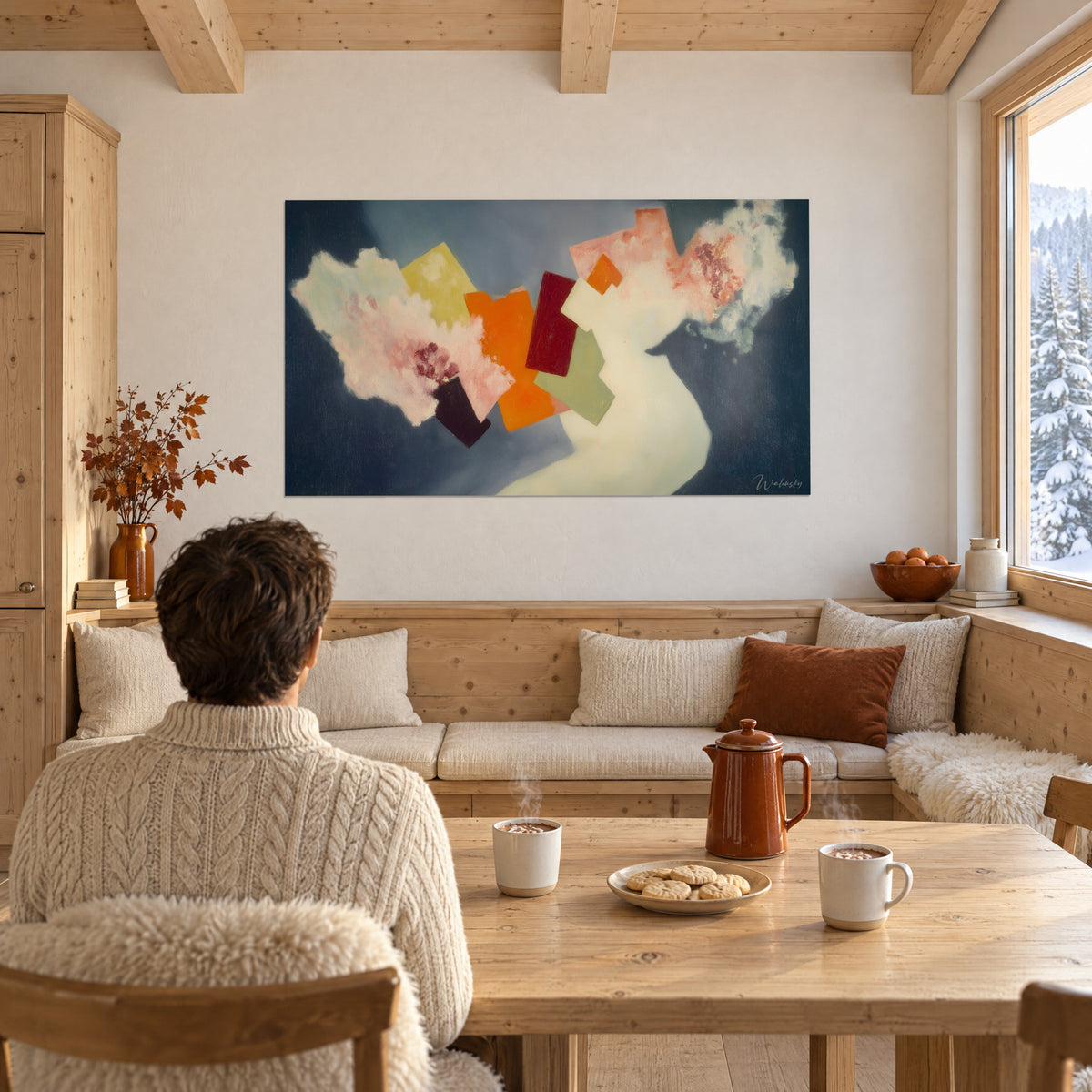 Quadro collage di quadrati arancio, verde salvia e bordeaux, persona di spalle seduta a un tavolo di chalet in legno chiaro